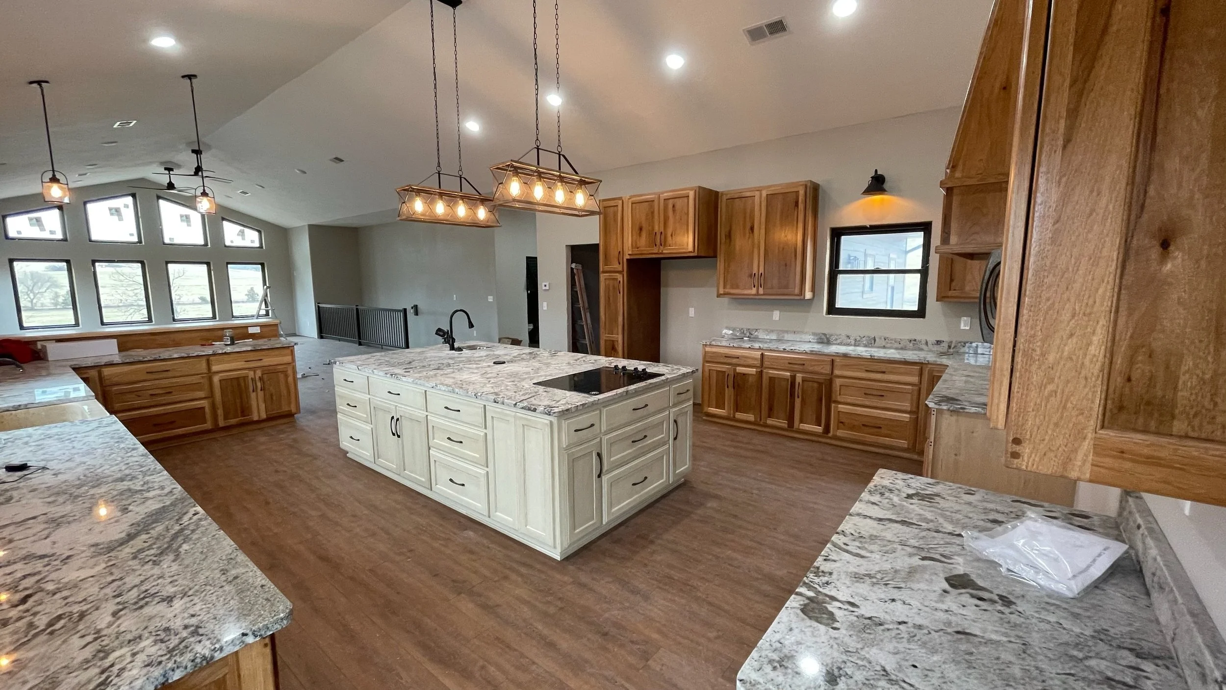 Modern open-concept kitchen with granite countertops, wooden cabinets, and large window overlooking a bright living area.