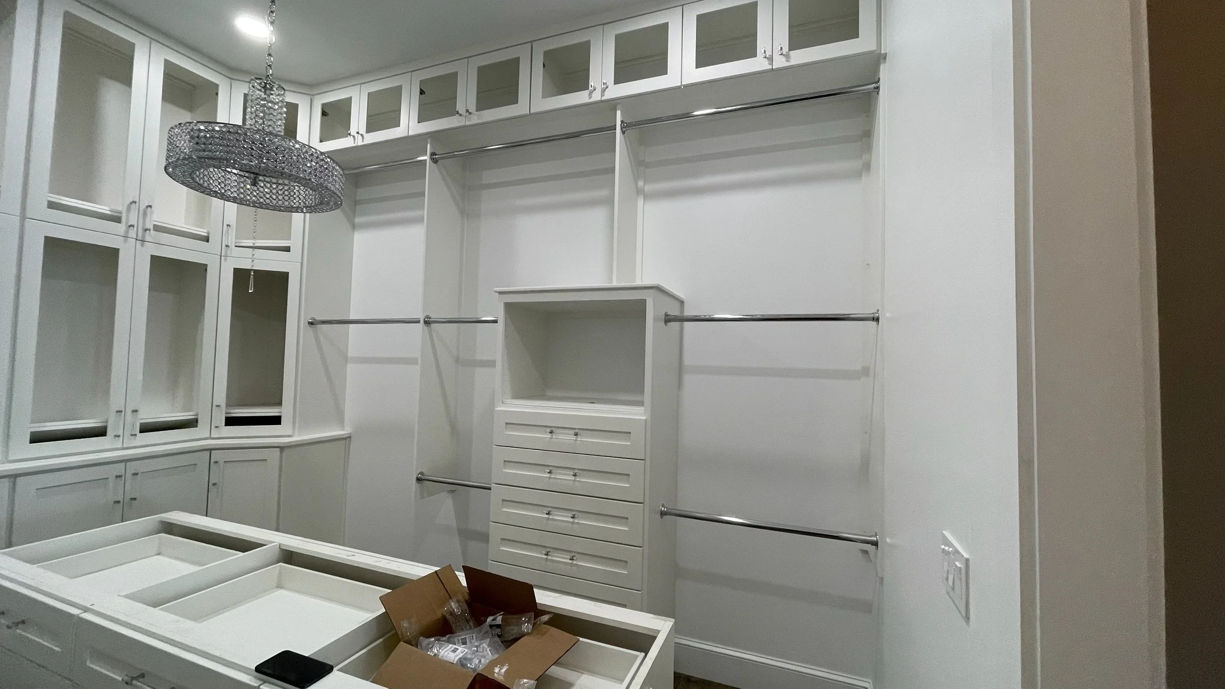 Empty walk-in closet with white cabinetry, multiple hanging rods, glass-front cabinets, and a chandelier