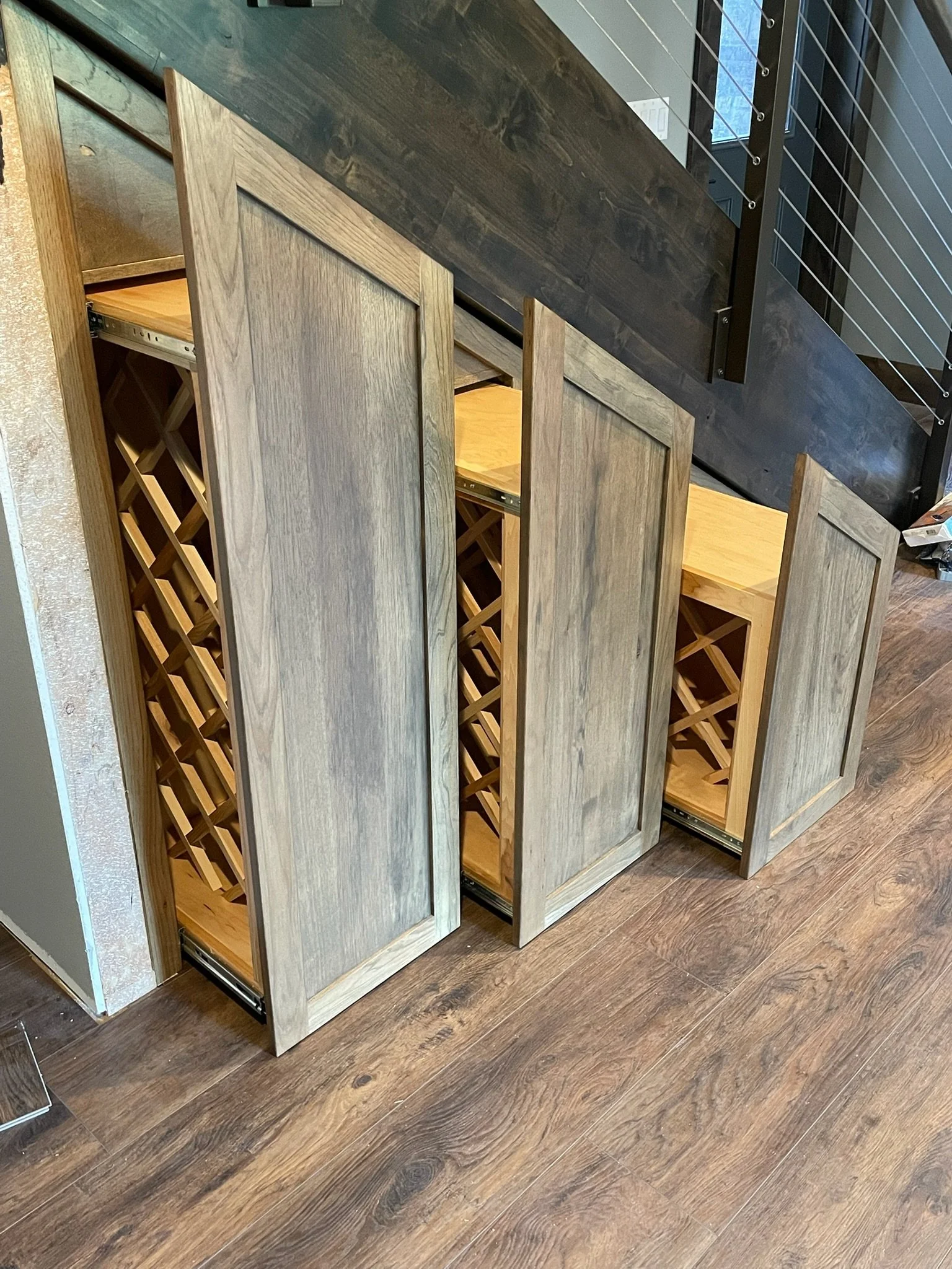 Wood wine rack cabinets with pull-out shelves in a room with a dark wood countertop and a metal railing.