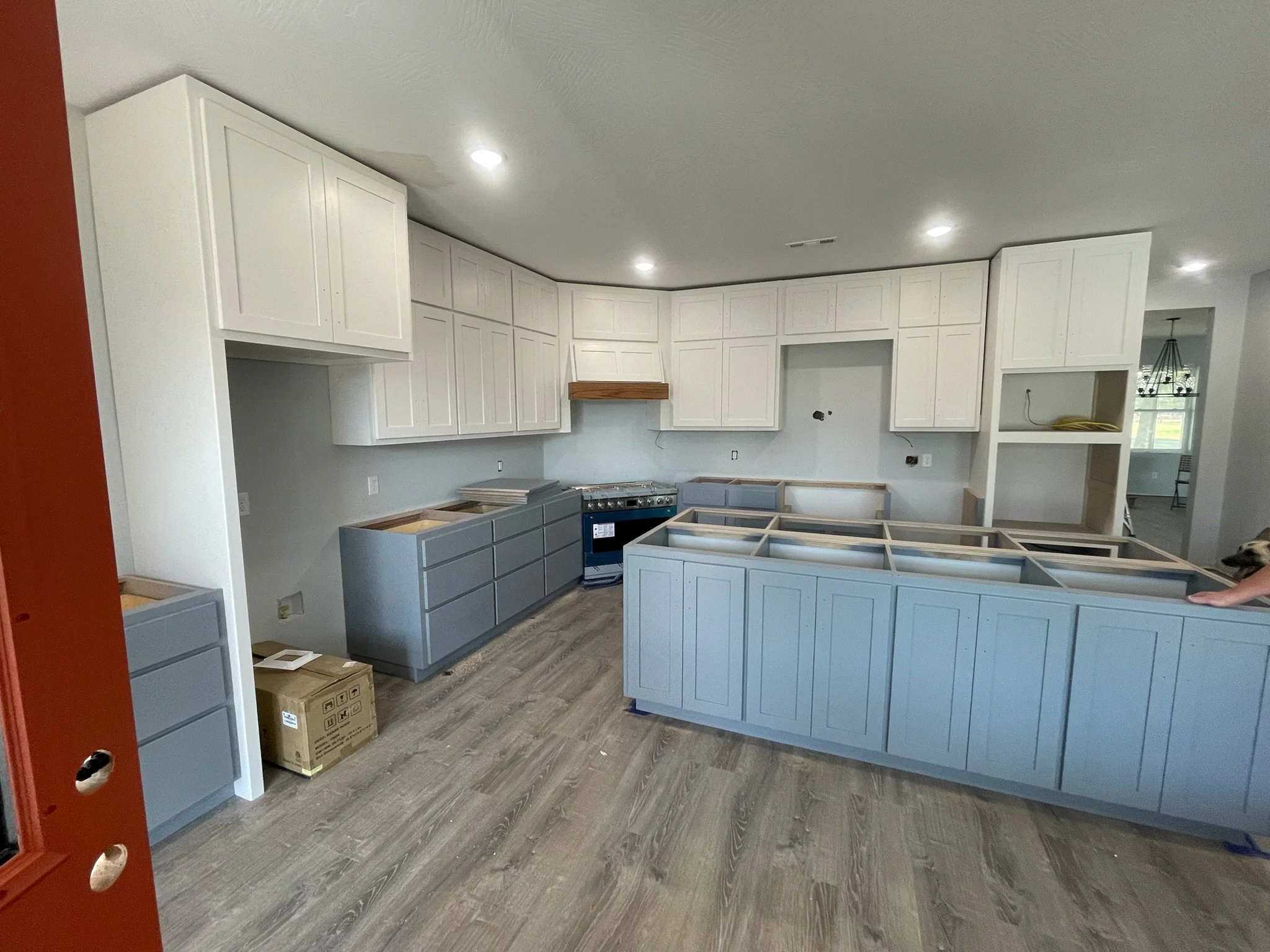 Kitchen under construction with white cabinets, some painted blue, and no countertops installed. There are boxes on the floor and a stove connecting the cabinets.