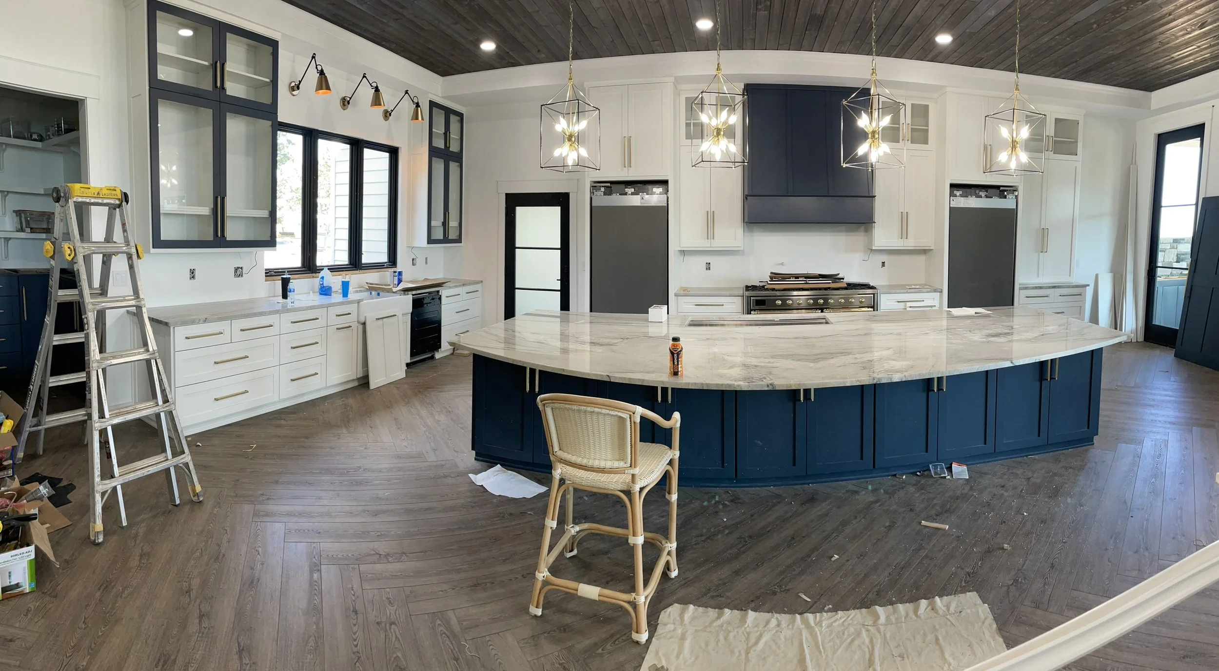 Kitchen under renovation with white and navy blue cabinets, a marble island, a ladder, and unfinished details.