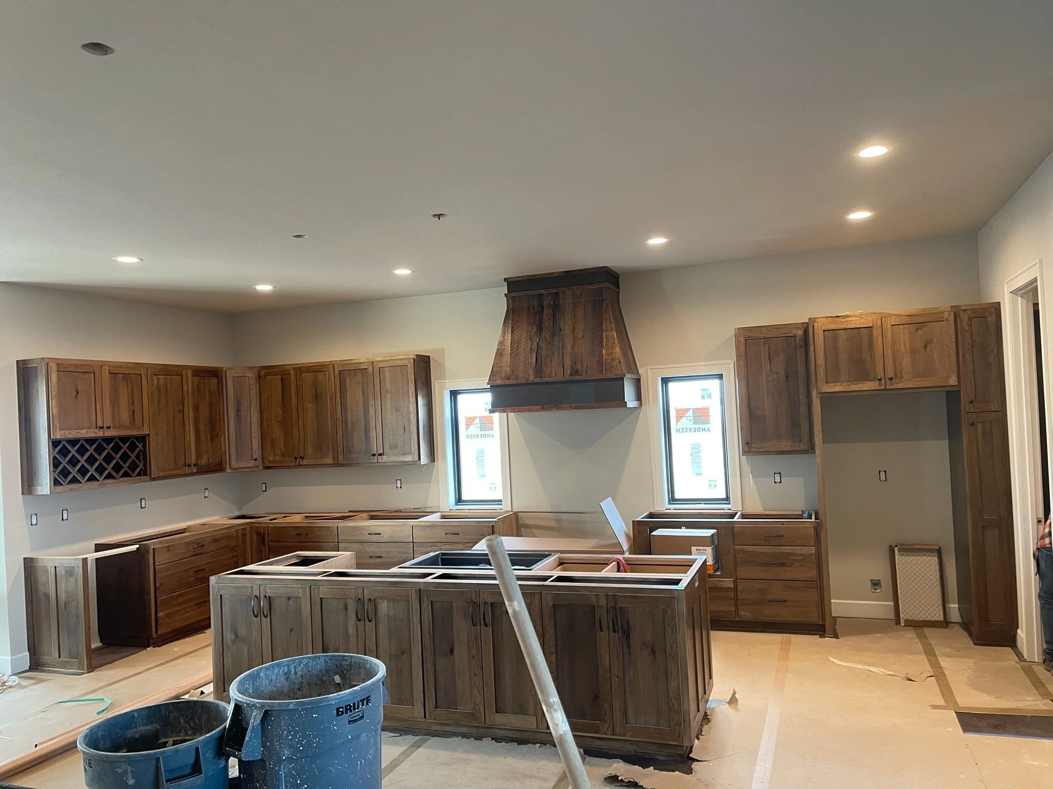 Kitchen under construction with wooden cabinets, a central island, windows, and a range hood.
