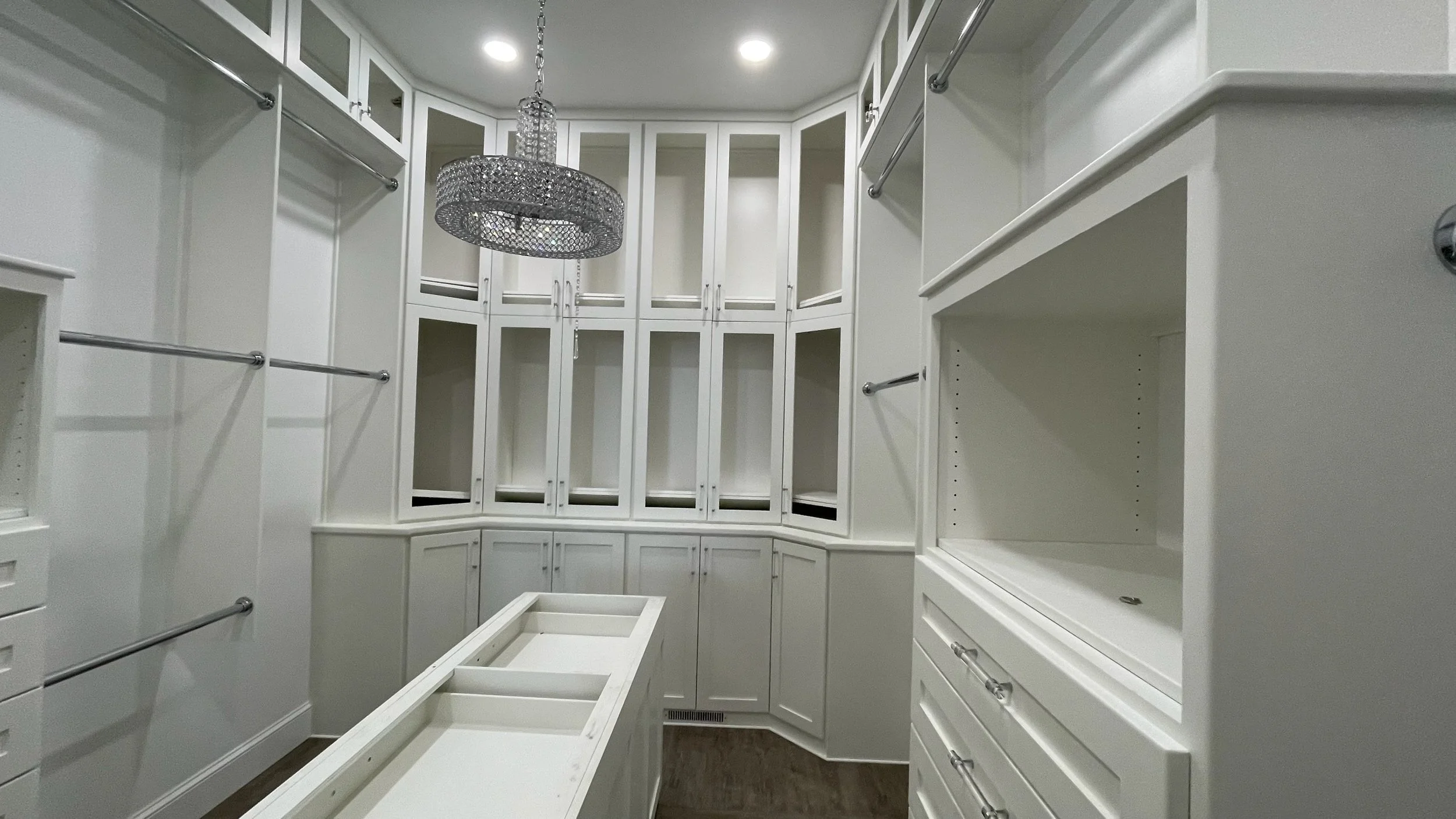 A spacious walk-in closet with white cabinetry, hanging rods, and a crystal chandelier.