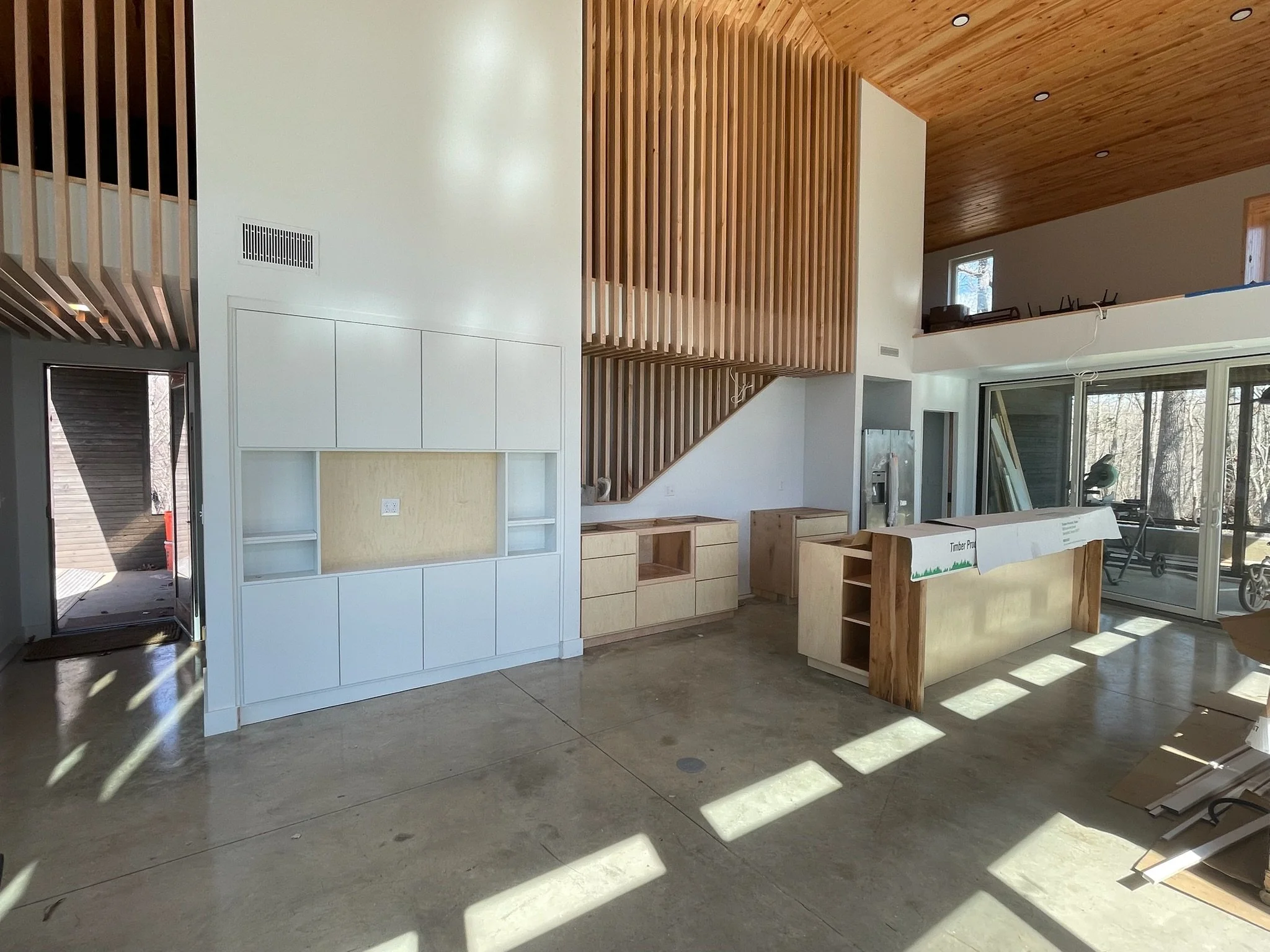 Interior of a house under construction with wooden cabinetry, a staircase, and large sliding glass doors.