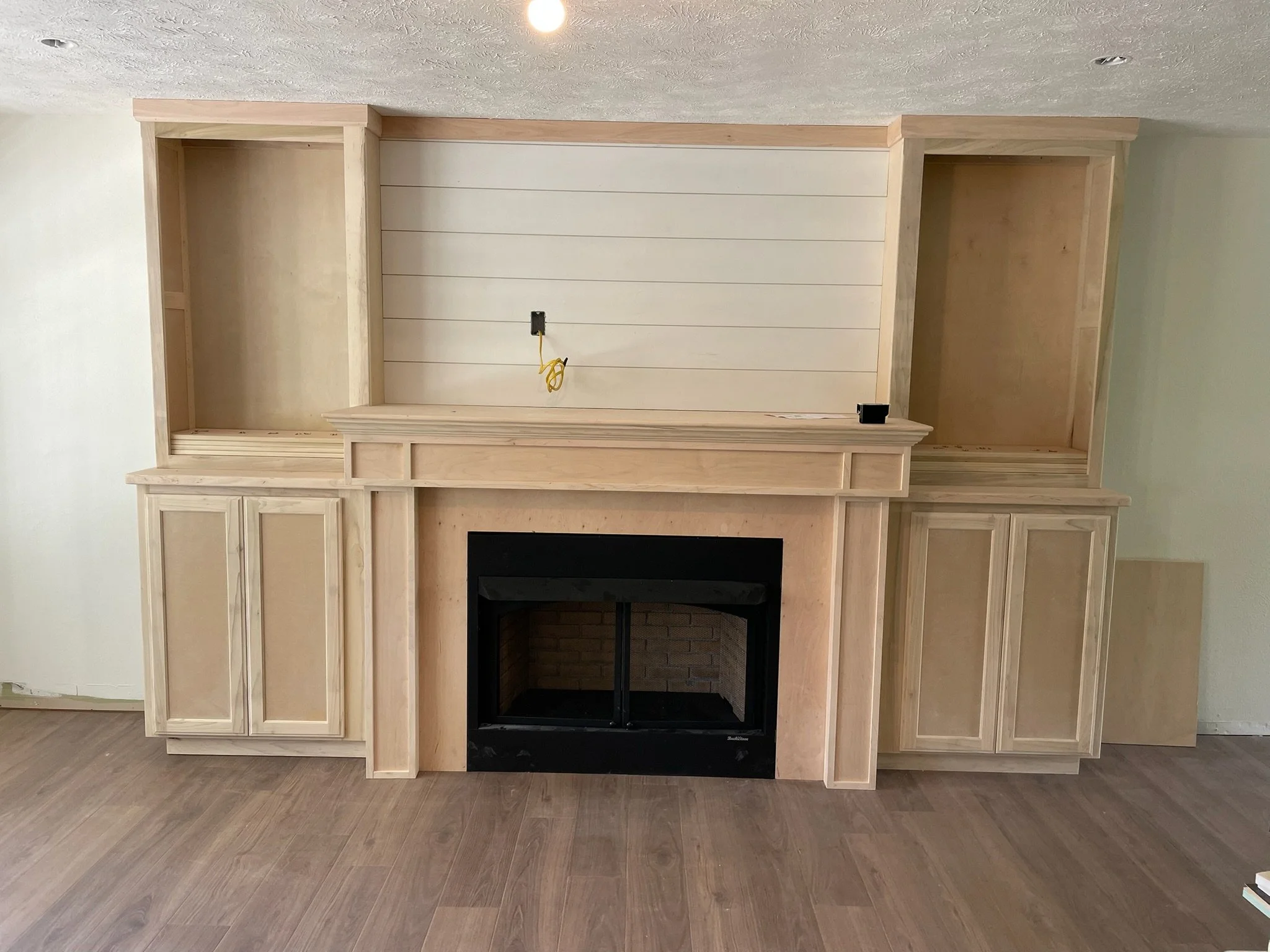 Construction of a built-in wood fireplace with cabinets on either side in a living room, with electrical wiring visible and no finished shelves or mantel yet.