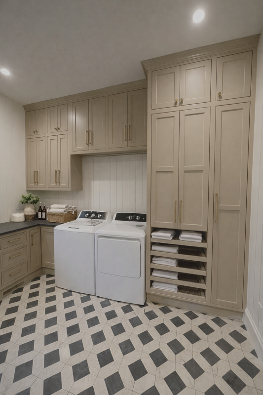 Laundry room with beige cabinets, a white washer and dryer, and a black and white diamond-patterned tile floor.
