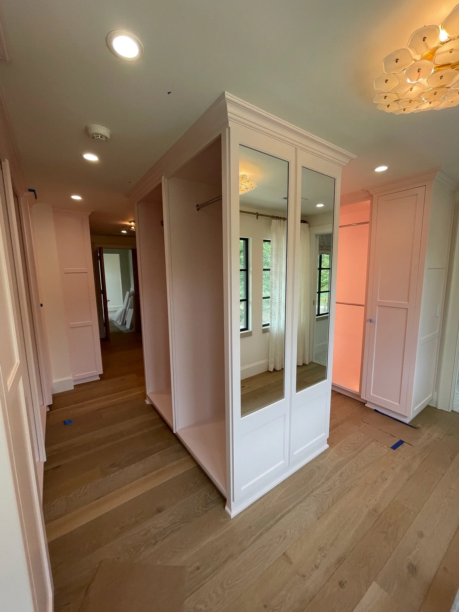 Interior of a house under construction featuring a white built-in wardrobe with mirrored doors, hardwood flooring, and multiple ceiling lights.