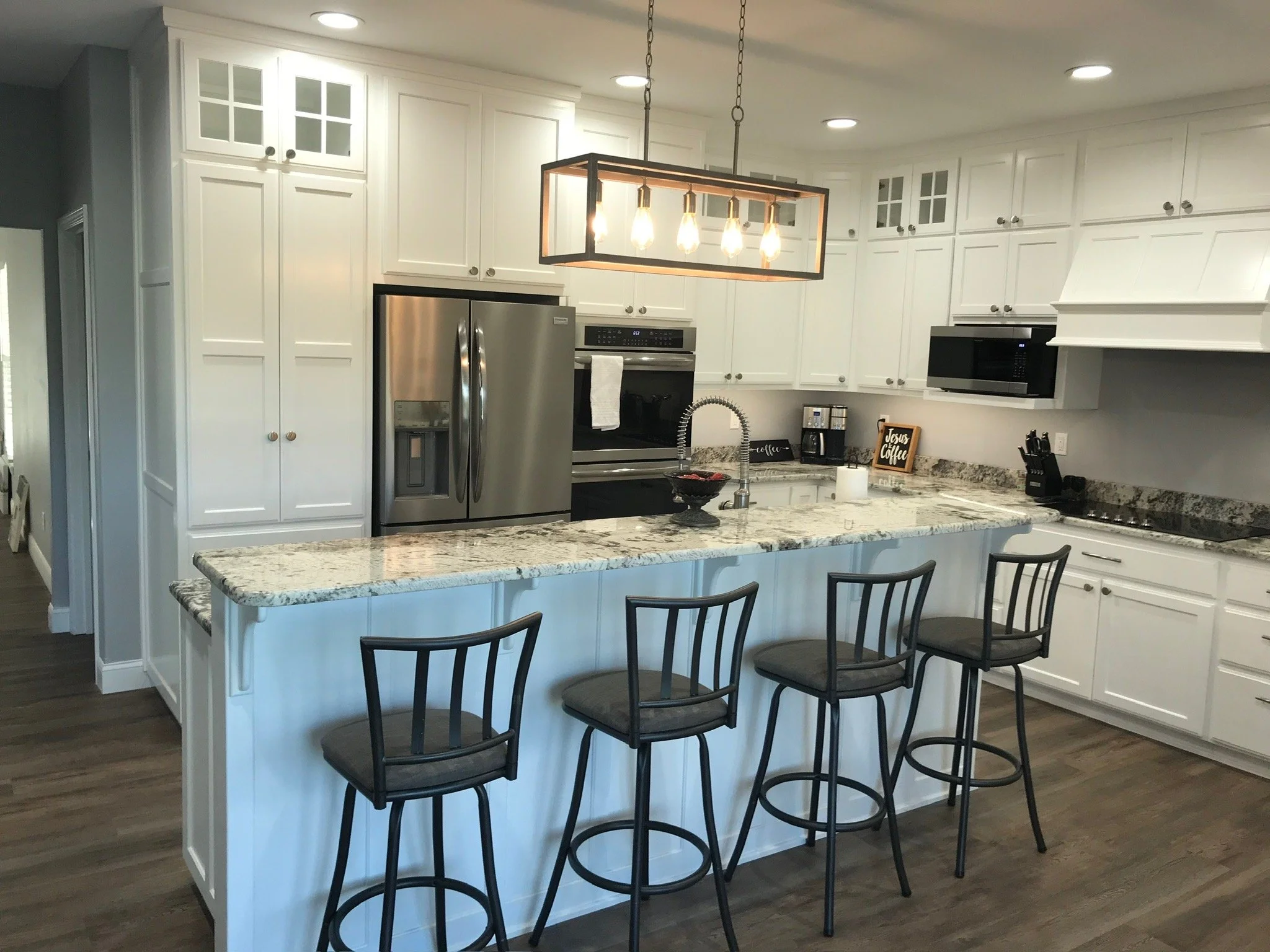 Modern kitchen with white cabinetry, granite countertops, stainless steel refrigerator, oven, microwave, and black bar stools around a kitchen island.