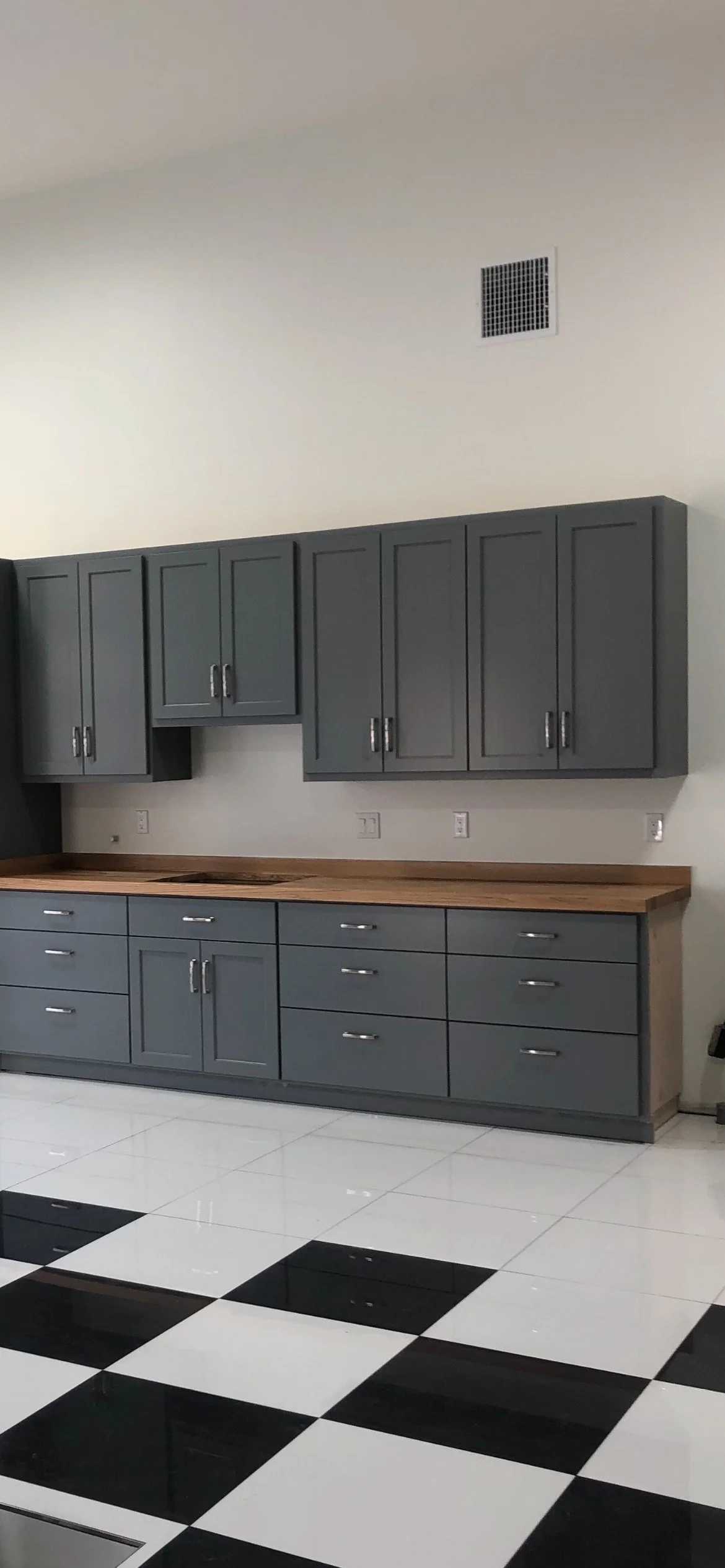 Kitchen with black and white checkered tile floor, gray cabinets, and a wooden countertop.