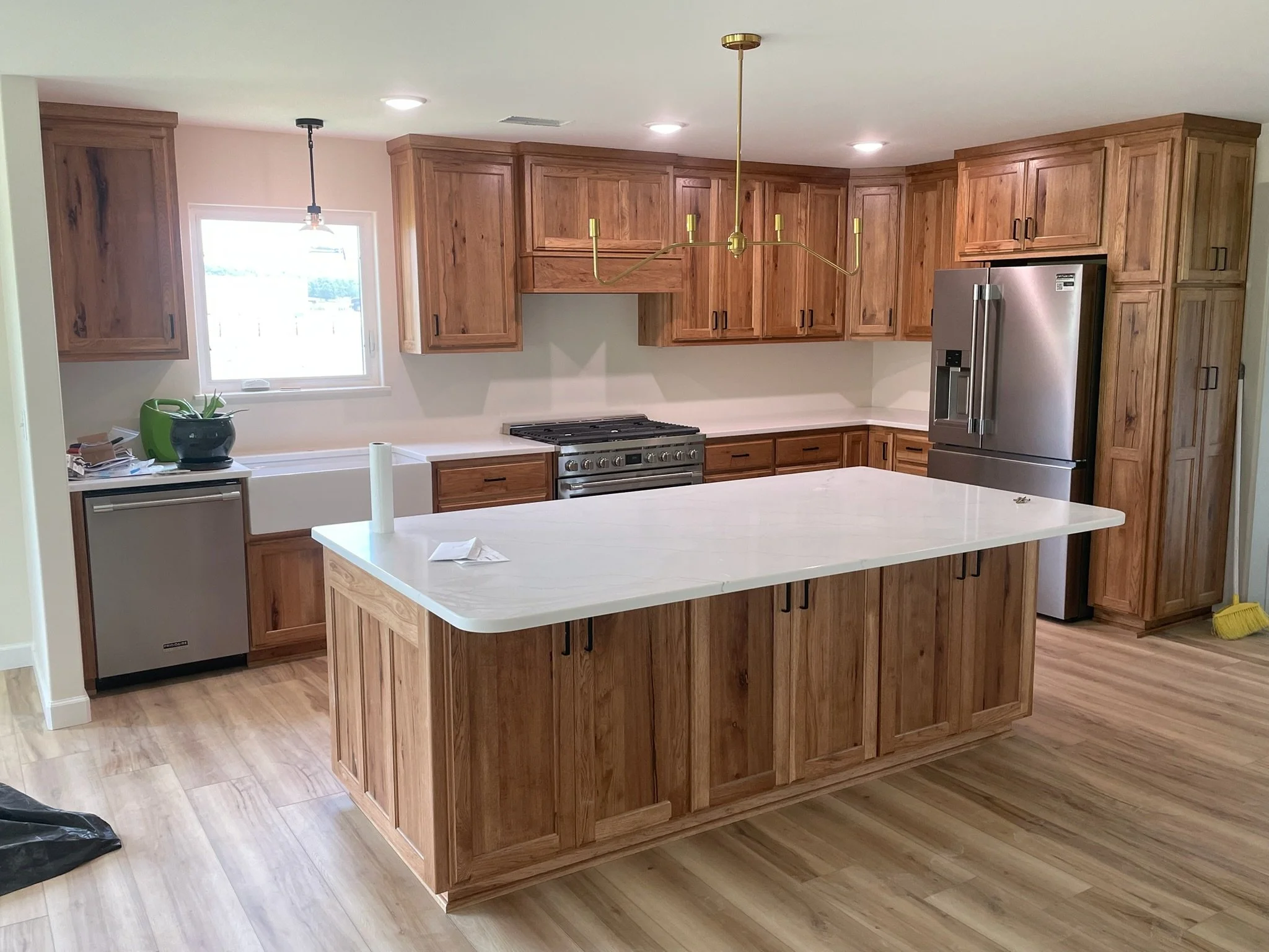 A modern kitchen with wooden cabinets, stainless steel appliances, a large white island in the center, and laminate wood flooring.