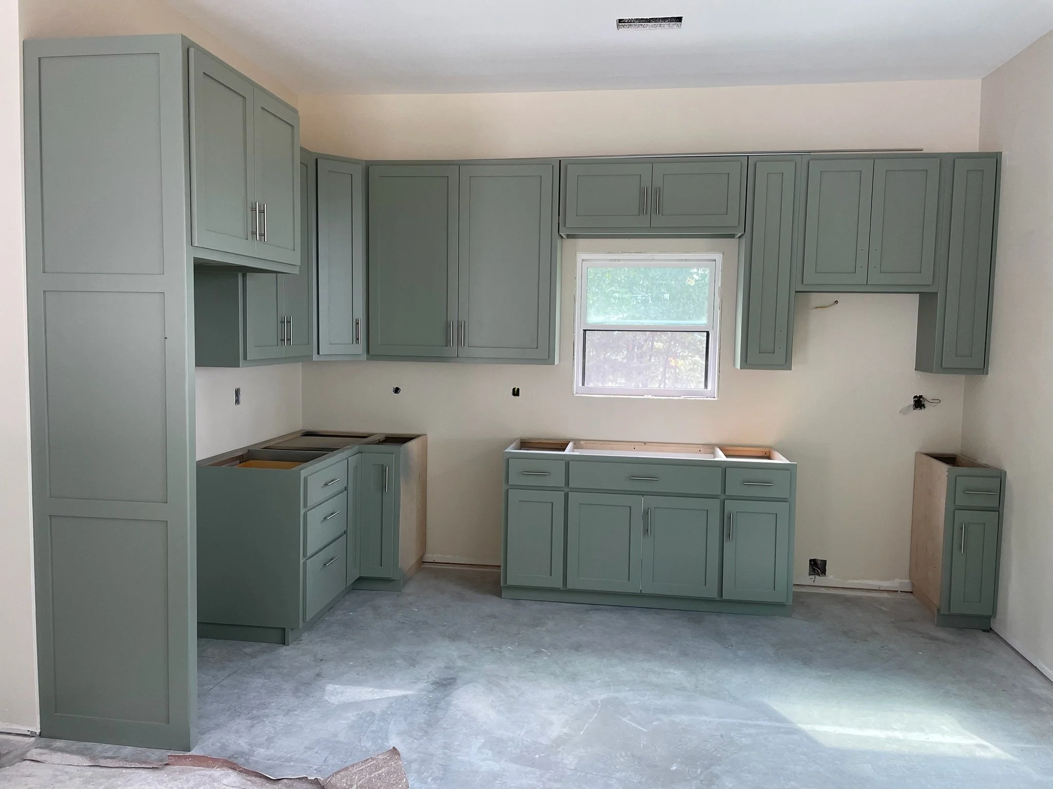 Kitchen under construction with green cabinets, a window, and unfinished countertops.