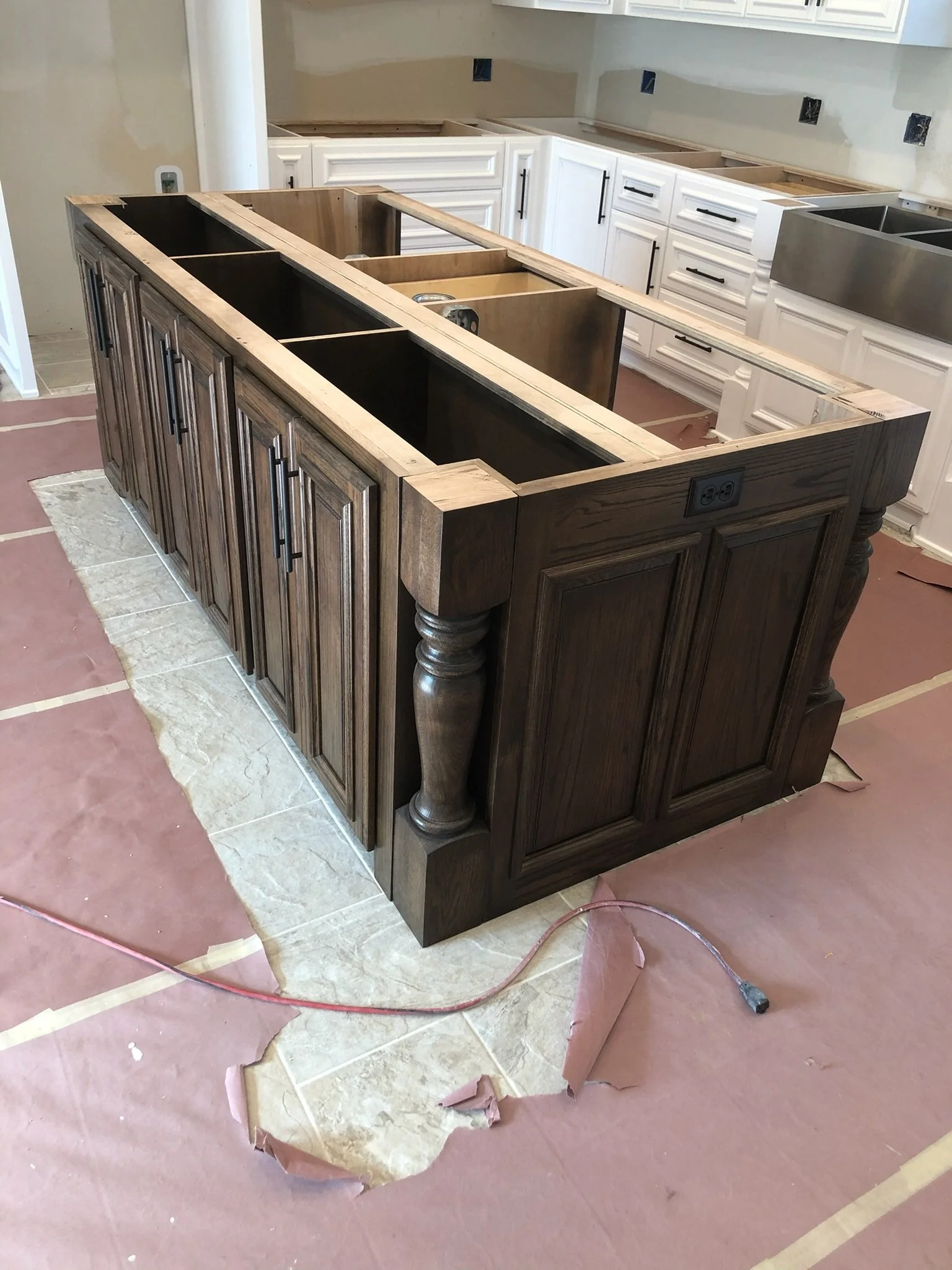 Kitchen island under construction with a wooden base, electrical outlets, and no countertop, surrounded by brown paper and construction materials.