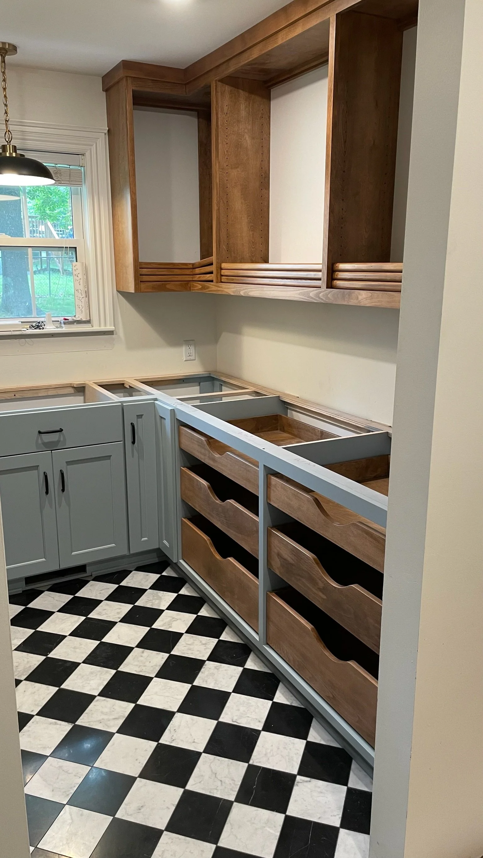 A kitchen under renovation with light blue cabinets, wooden drawers, and black and white checkered flooring.