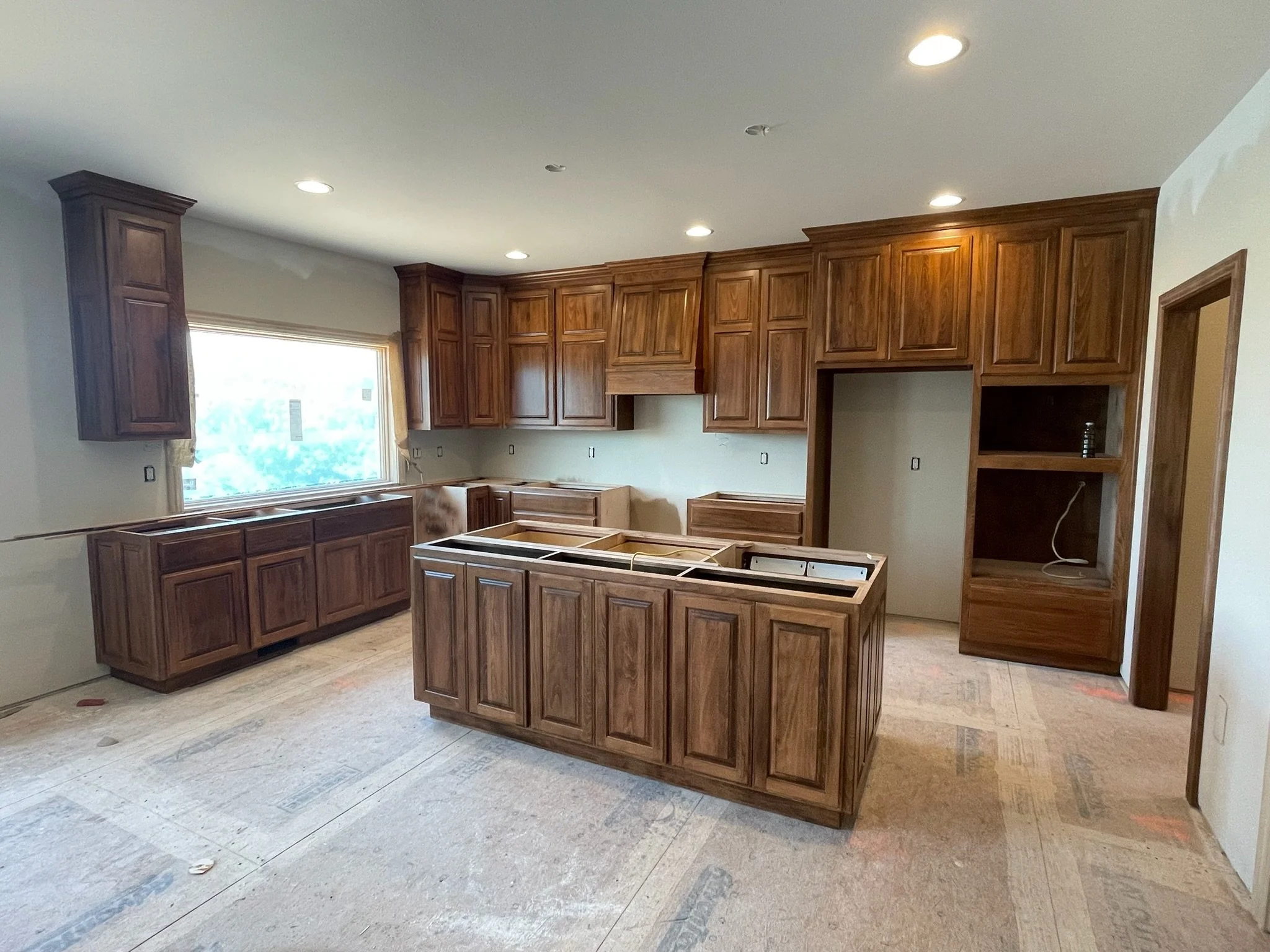 Kitchen with dark wood cabinets and an unfinished island, under construction.