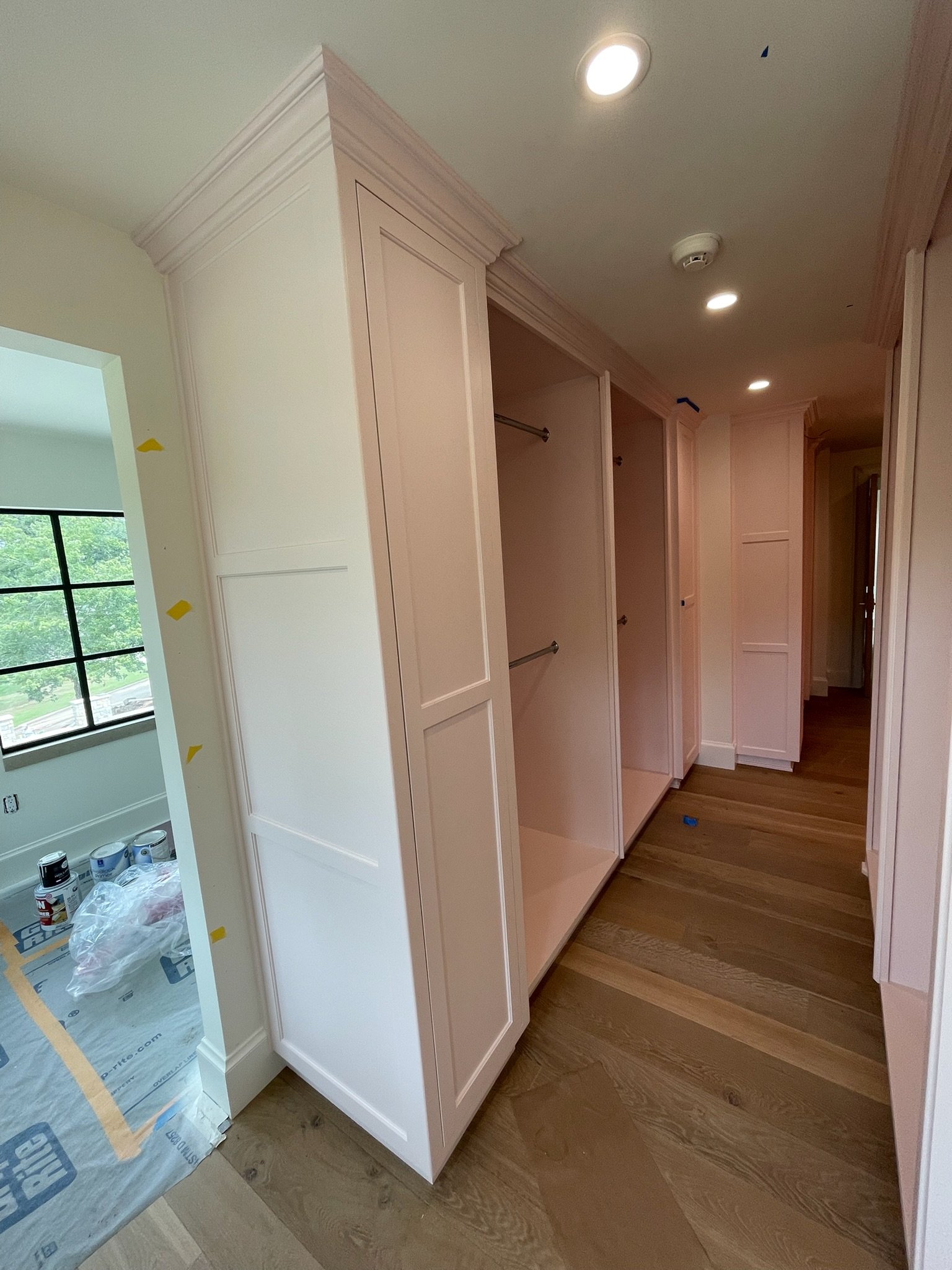 Unfinished built-in closet with open shelving and hanging rods in a residential room, with hardwood flooring and ceiling recessed lights.