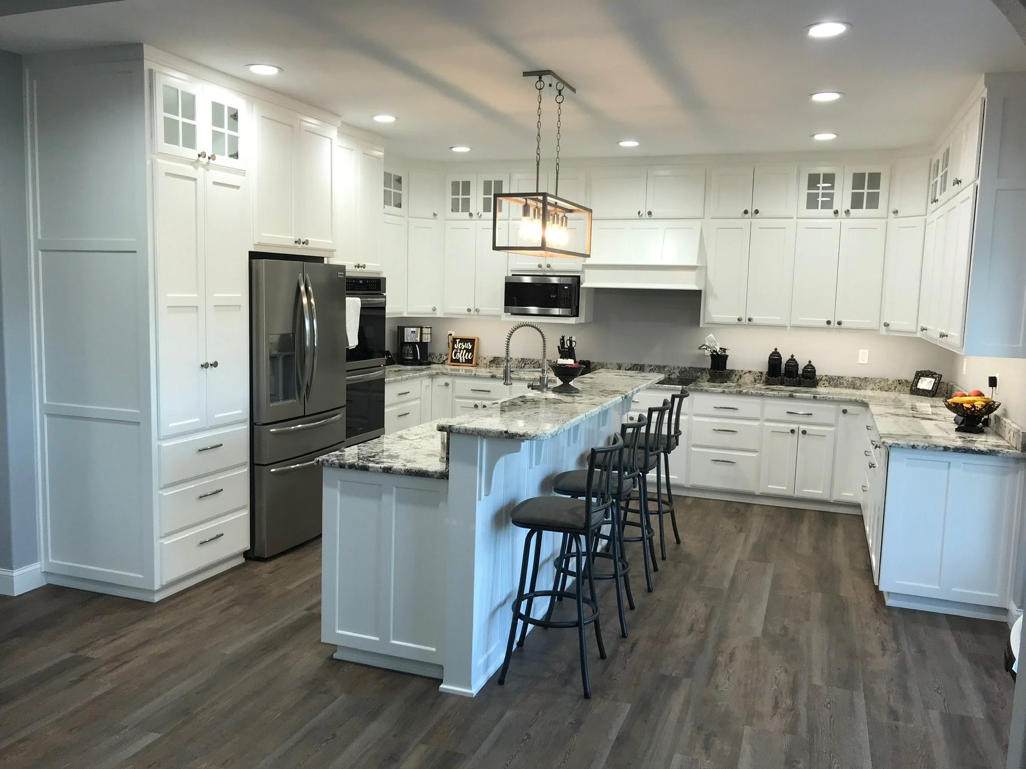 Modern white kitchen with granite countertops, stainless steel appliances, and black bar stools.