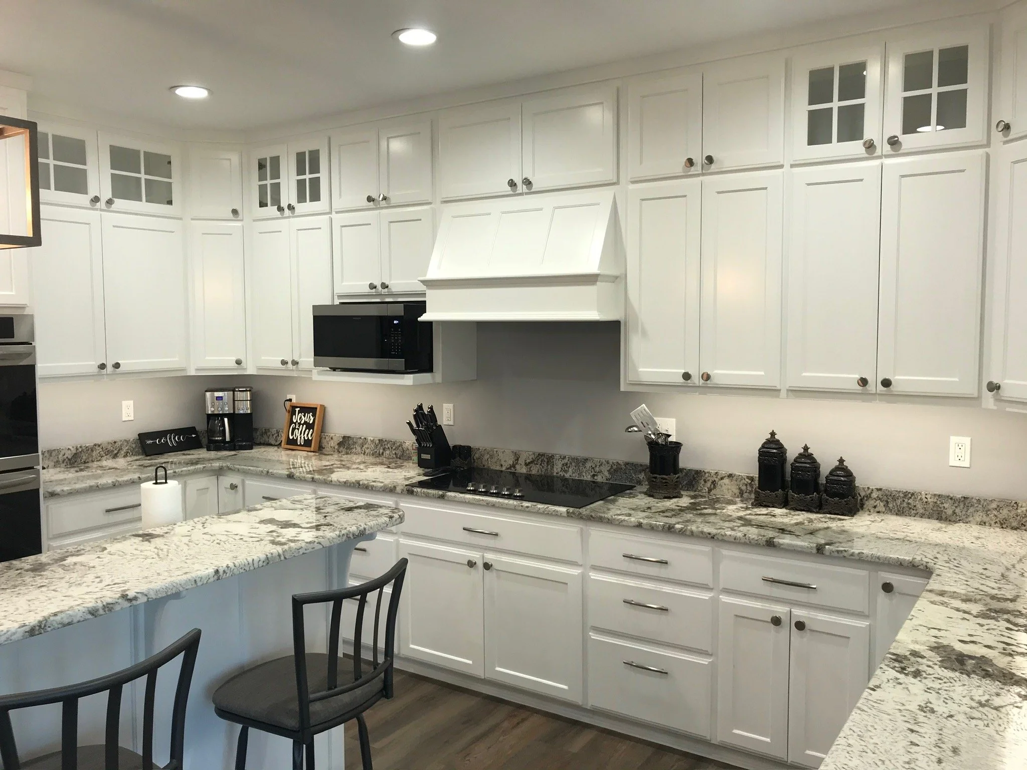 Kitchen with white cabinets, granite countertops, black appliances, coffee maker, knife block, black decorative jars, and bar stool.