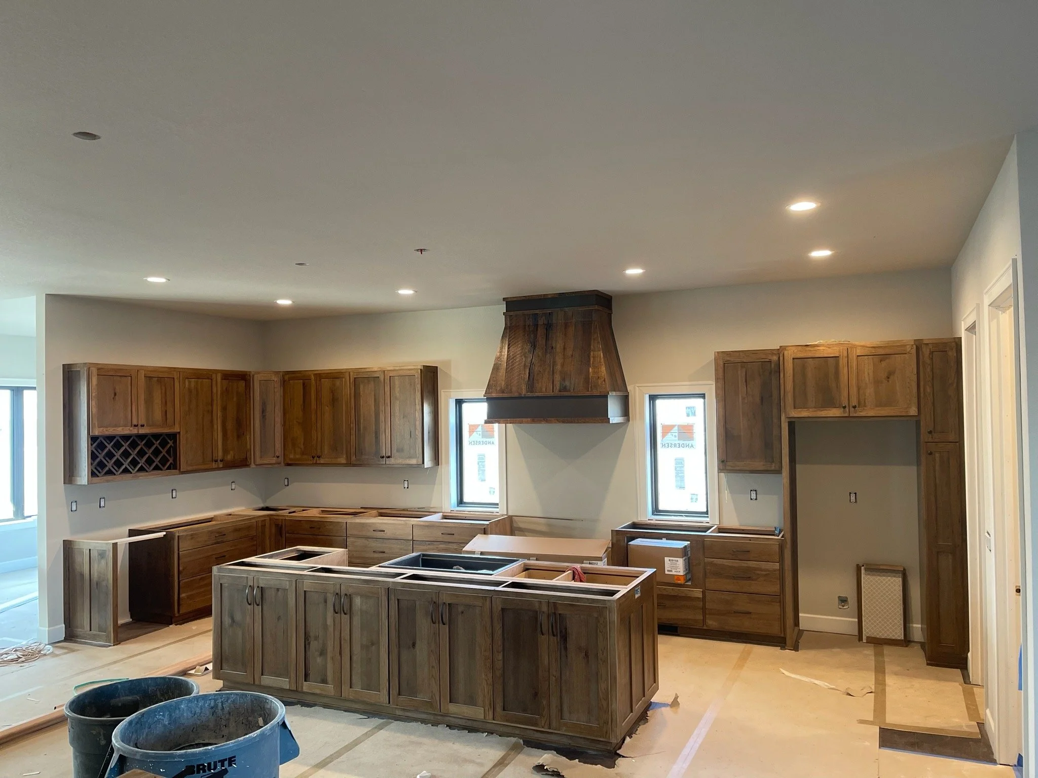 Kitchen under construction with wooden cabinets, a range hood, and empty spaces for appliances, during renovation.