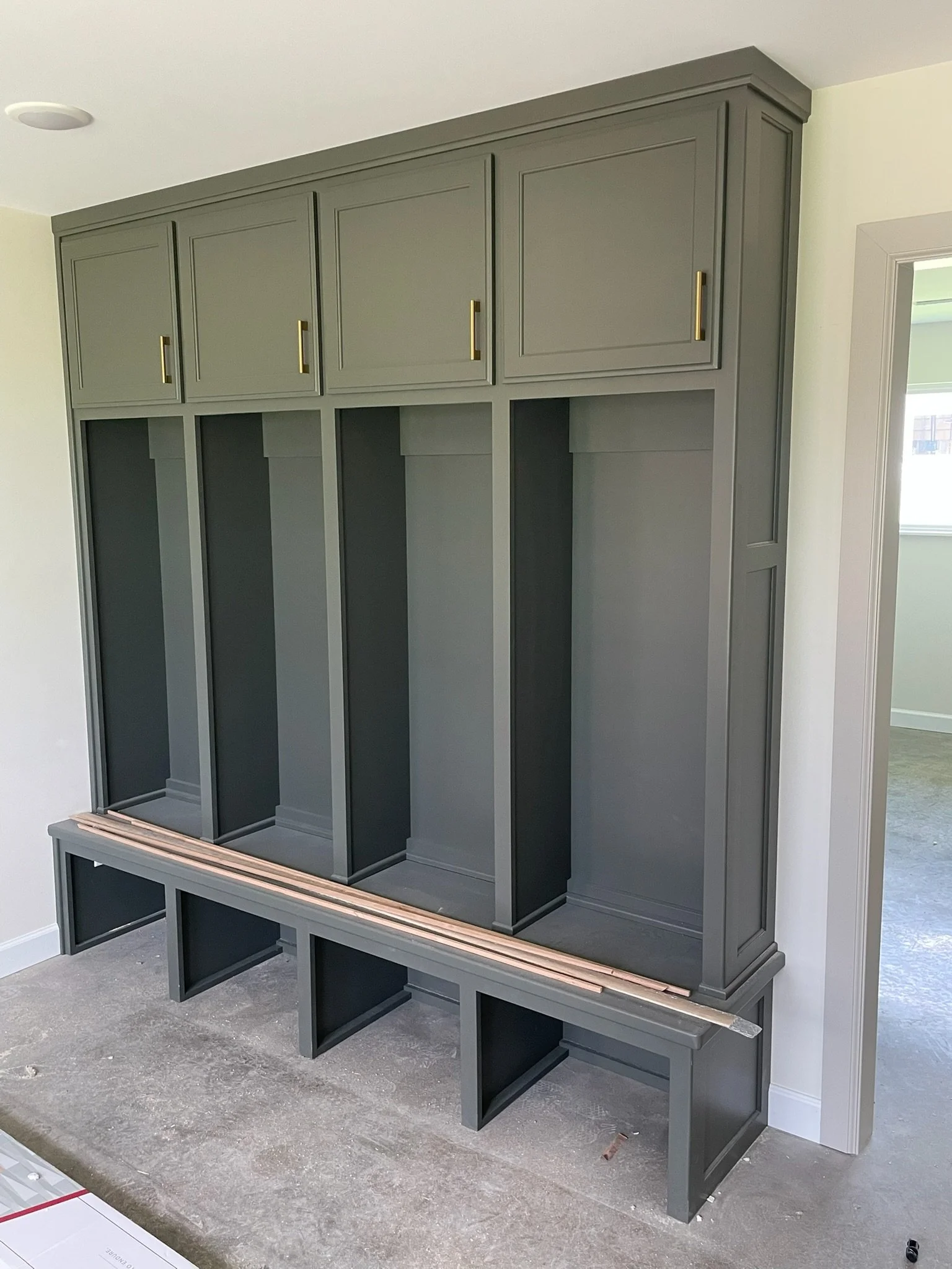 A partially assembled built-in closet or storage unit in a room with light-colored walls. The unit features cabinets with gold handles on the upper section, open compartments below, and a bench-like base with support legs. The floor appears to be und