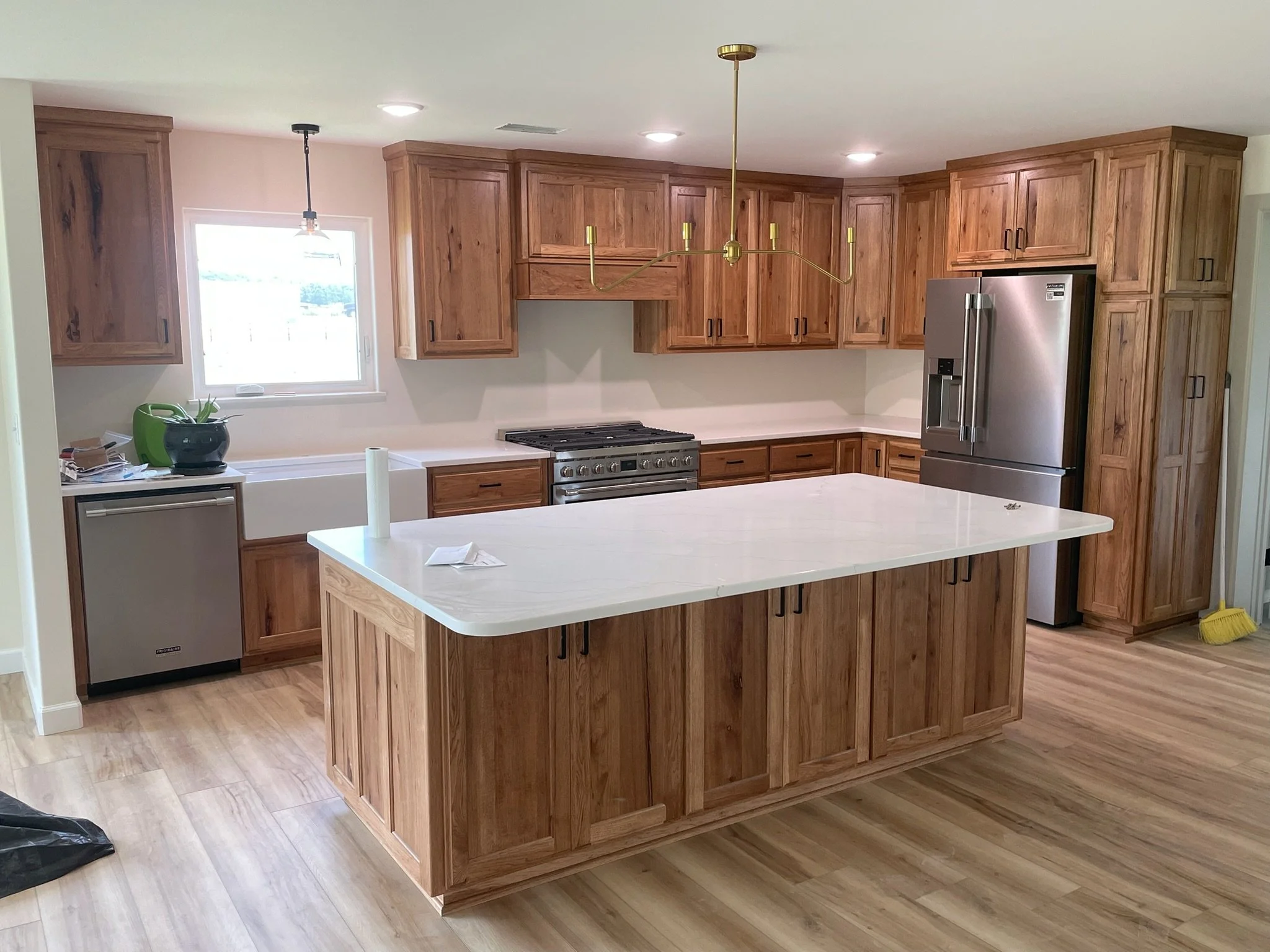Kitchen with wooden cabinets, white island, stainless steel refrigerator, range, window, and hardwood floors.