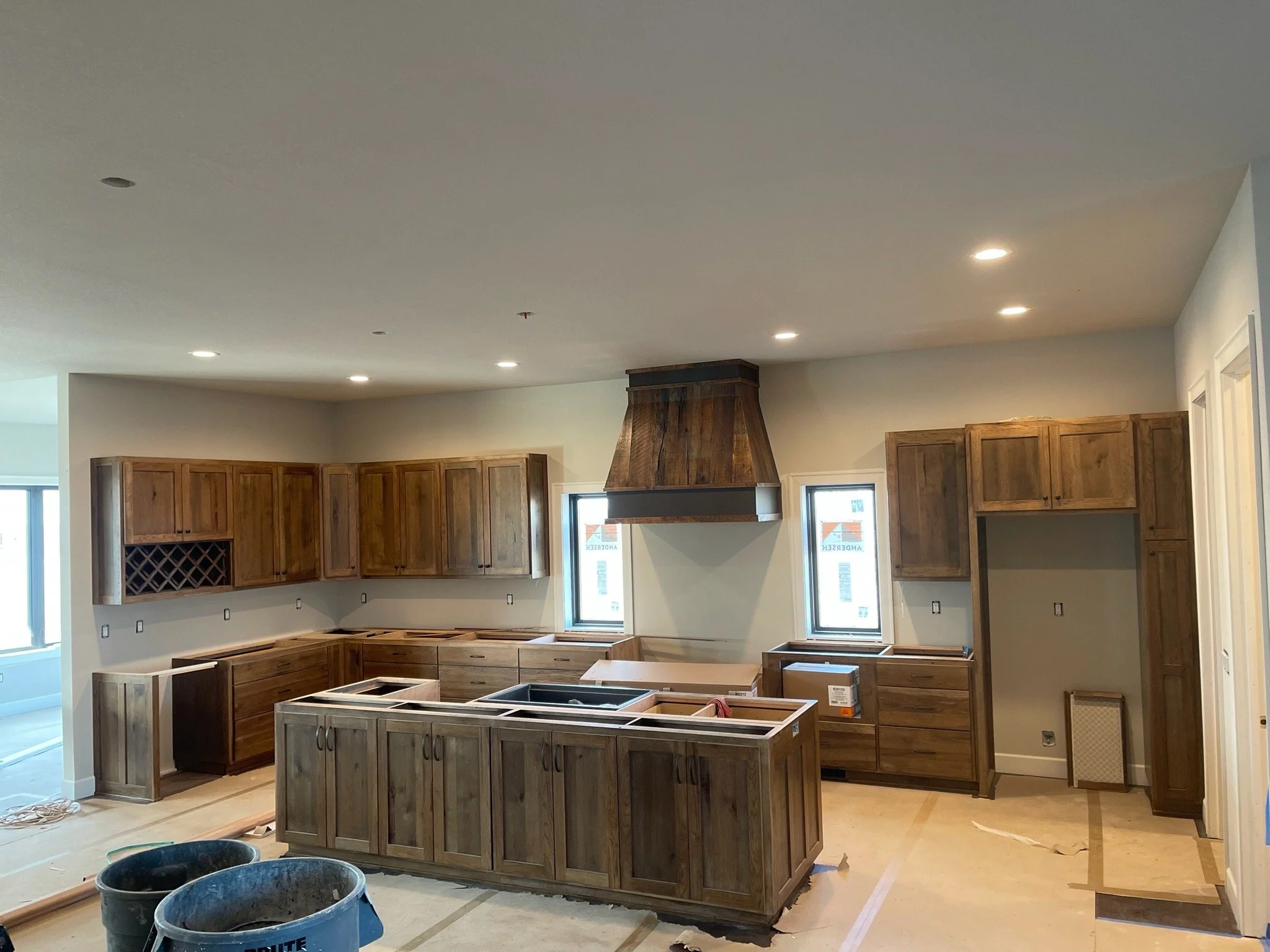 Kitchen under construction with wooden cabinets, a range hood, and unfinished counters, during daylight.