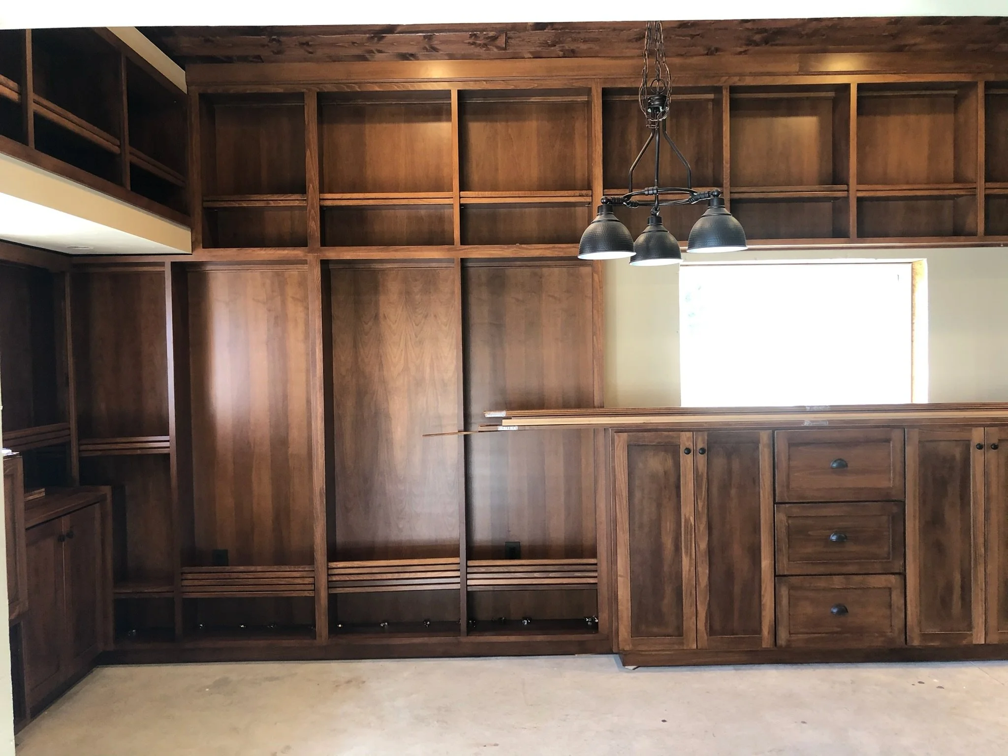 Empty wooden kitchen cabinets and shelves with a small window and black pendant light fixture.