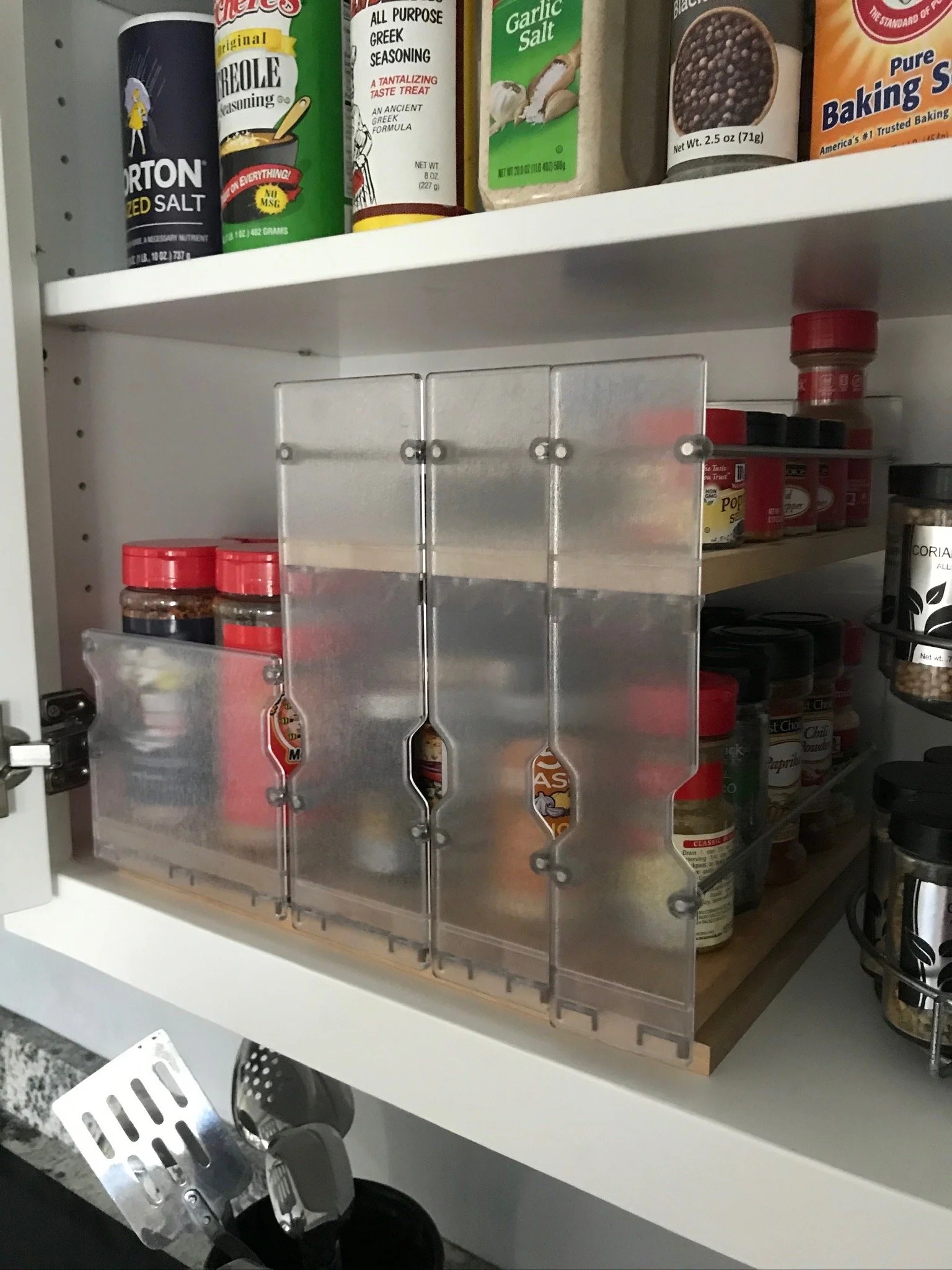 Open kitchen cabinet with spices and seasonings on the shelves, featuring a clear plastic spice container with multiple compartments.