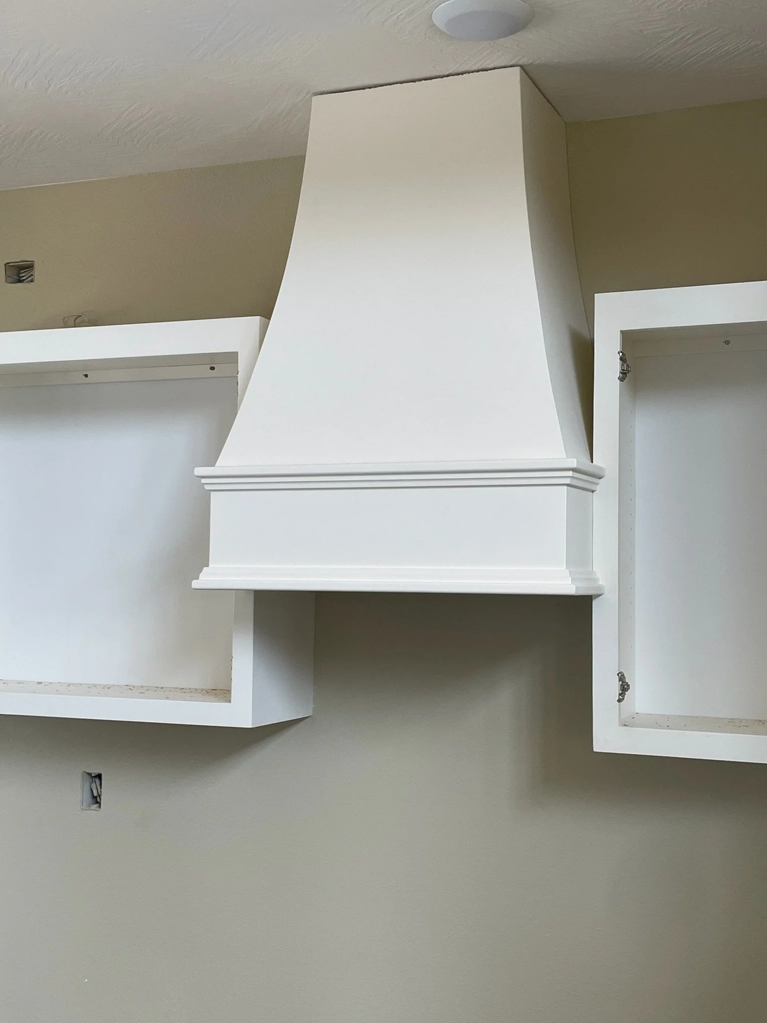 A white kitchen range hood mounted above empty white kitchen cabinets on a beige wall.