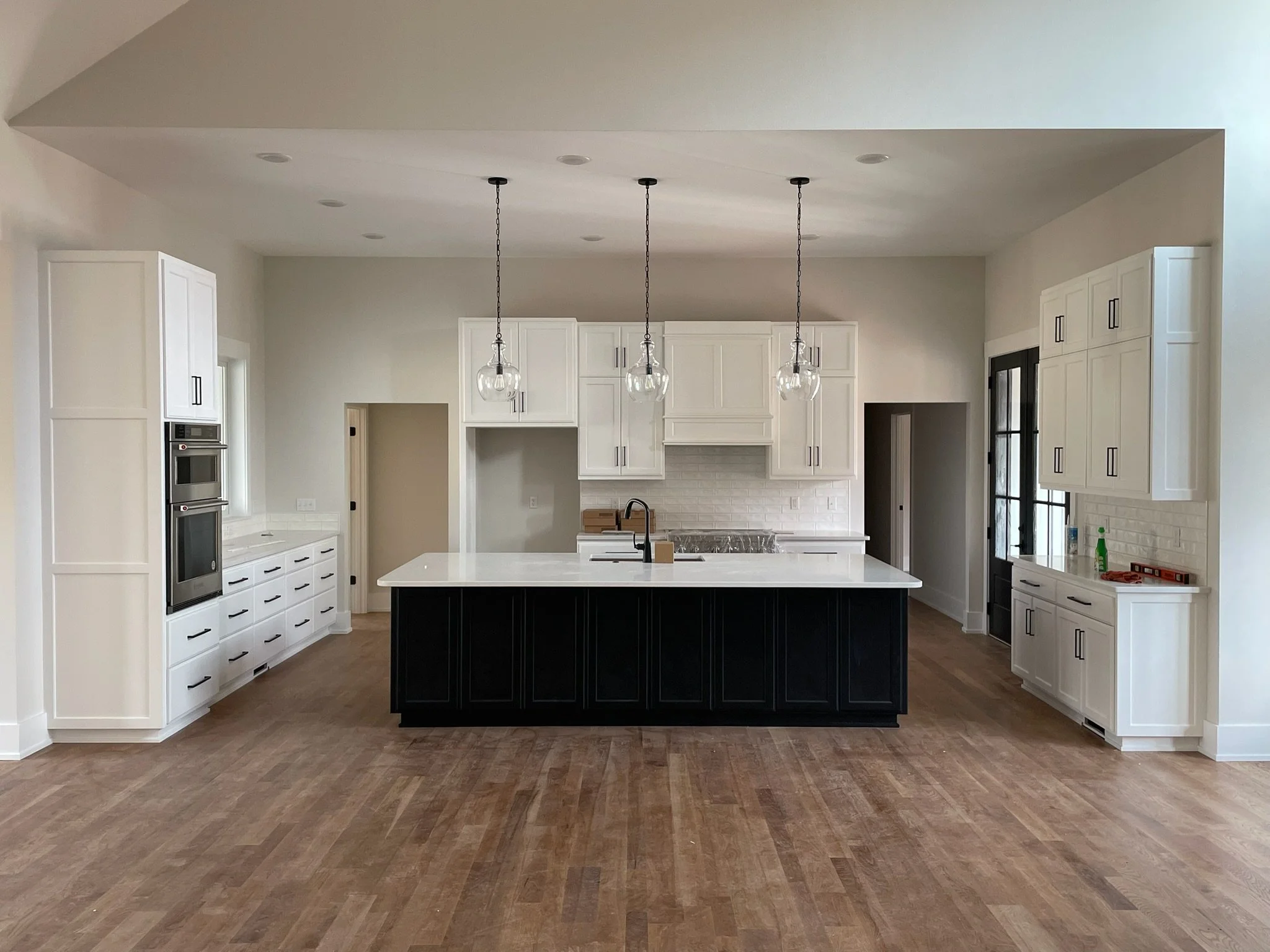 Modern kitchen with white cabinets, black island, pendant lights, hardwood floor, and a white subway tile backsplash.
