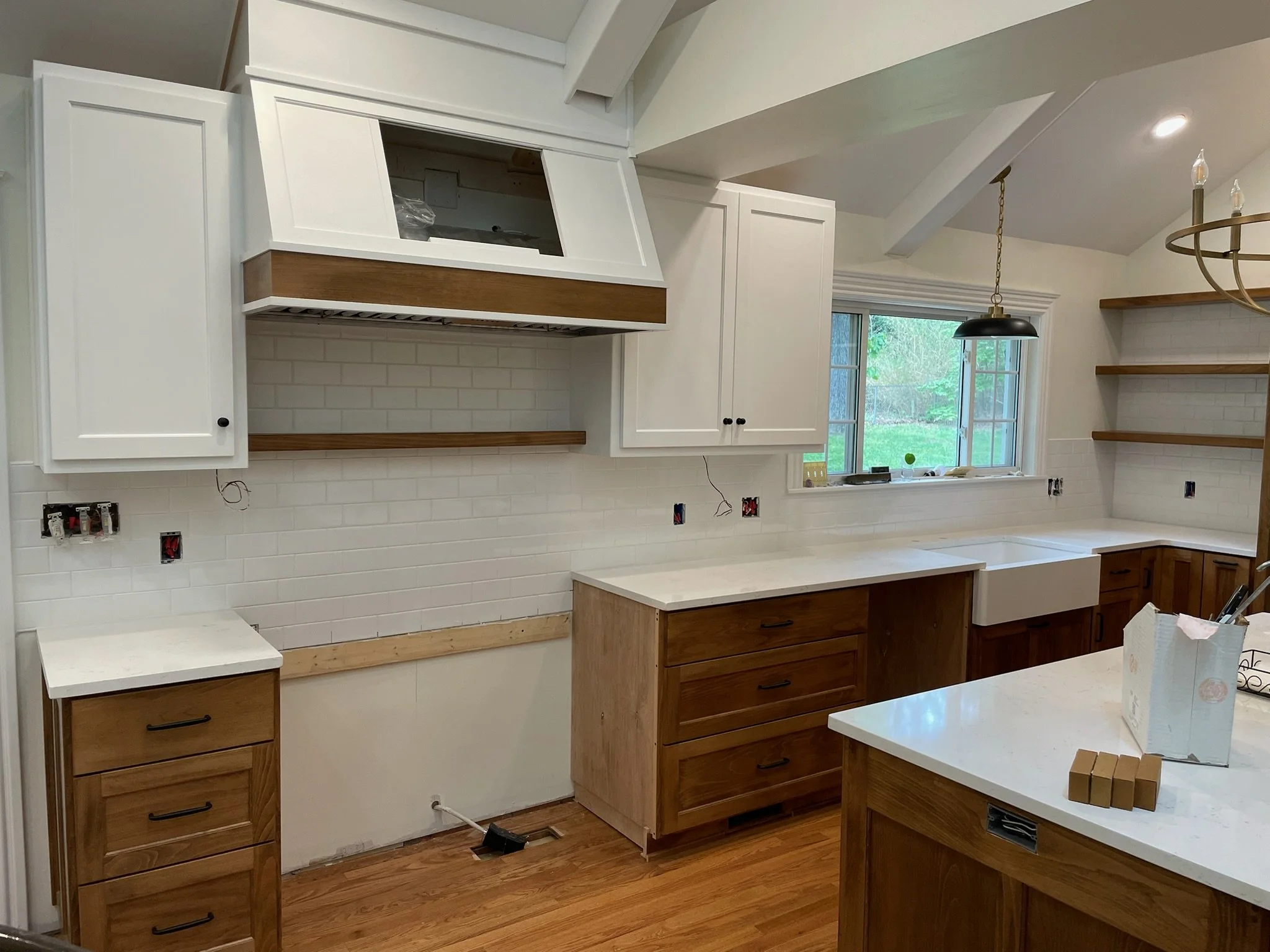 Kitchen under renovation with white upper cabinets, wooden lower cabinets, a white countertop, white subway tile backsplash, an empty space for a stove, and open shelves on the right side.