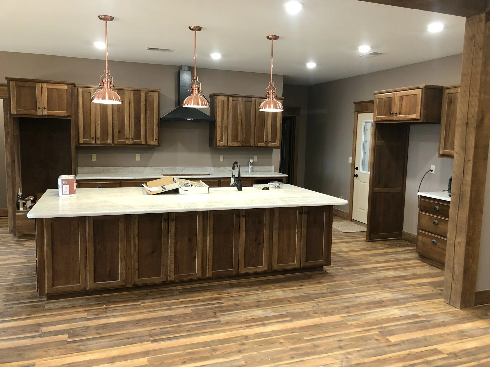 Kitchen with wooden cabinets and an island with a white countertop, three copper pendant lights above, and hardwood flooring.