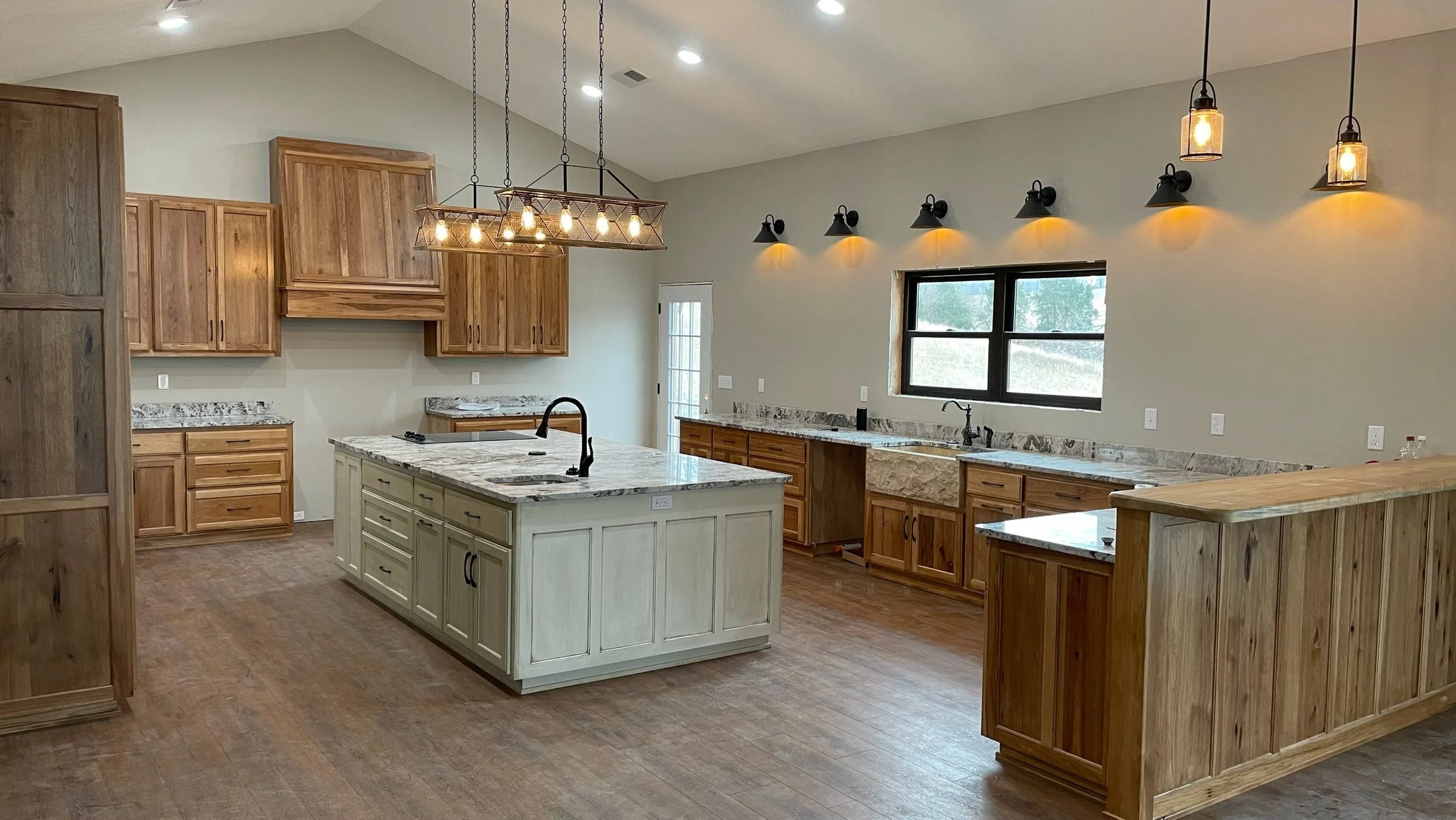 Modern kitchen with wooden cabinets, granite countertops, a center island, pendant and wall lighting, wood flooring, and a large window.