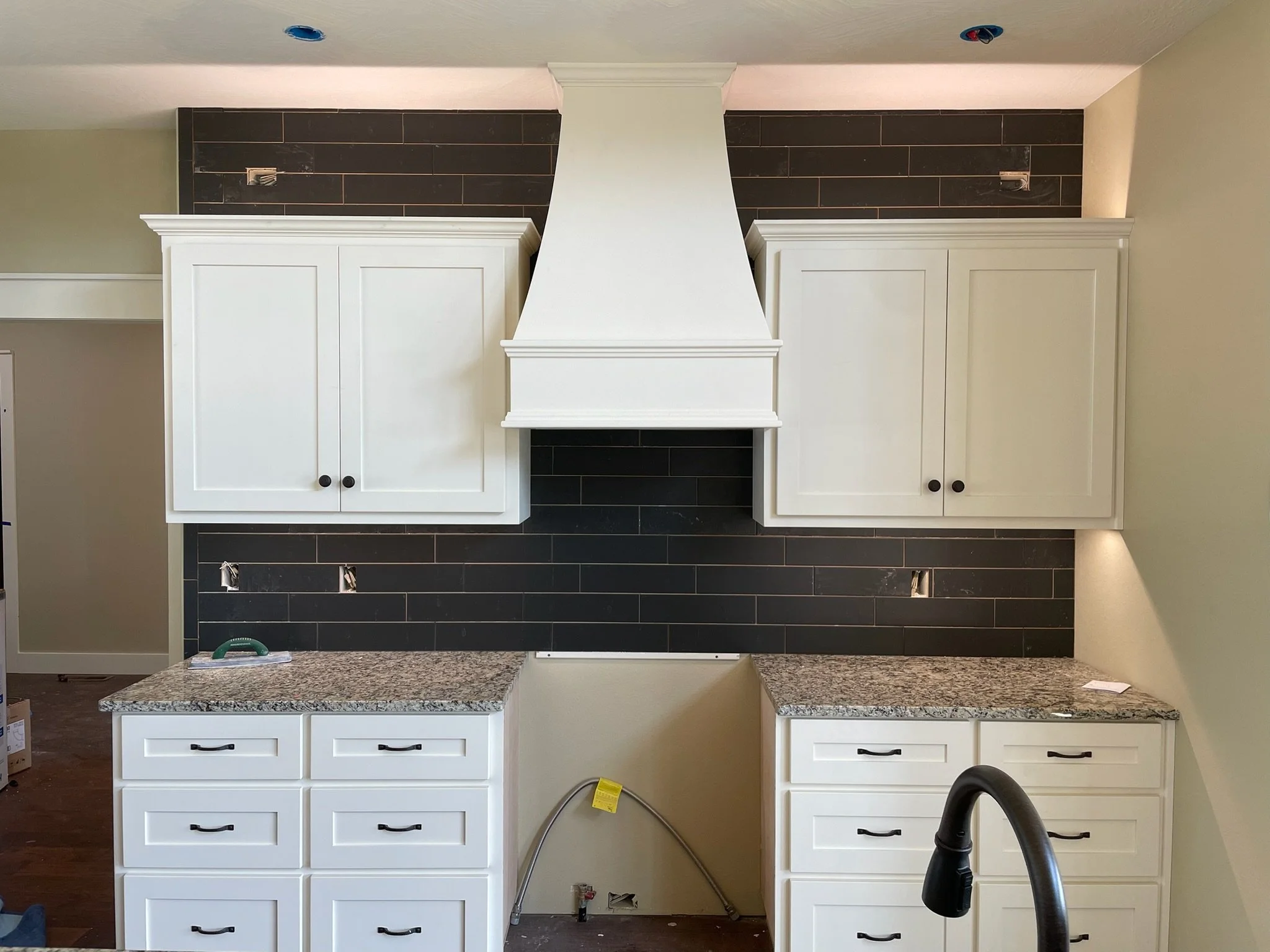 Under-construction kitchen with white cabinets, granite countertops, and black tiled backsplash