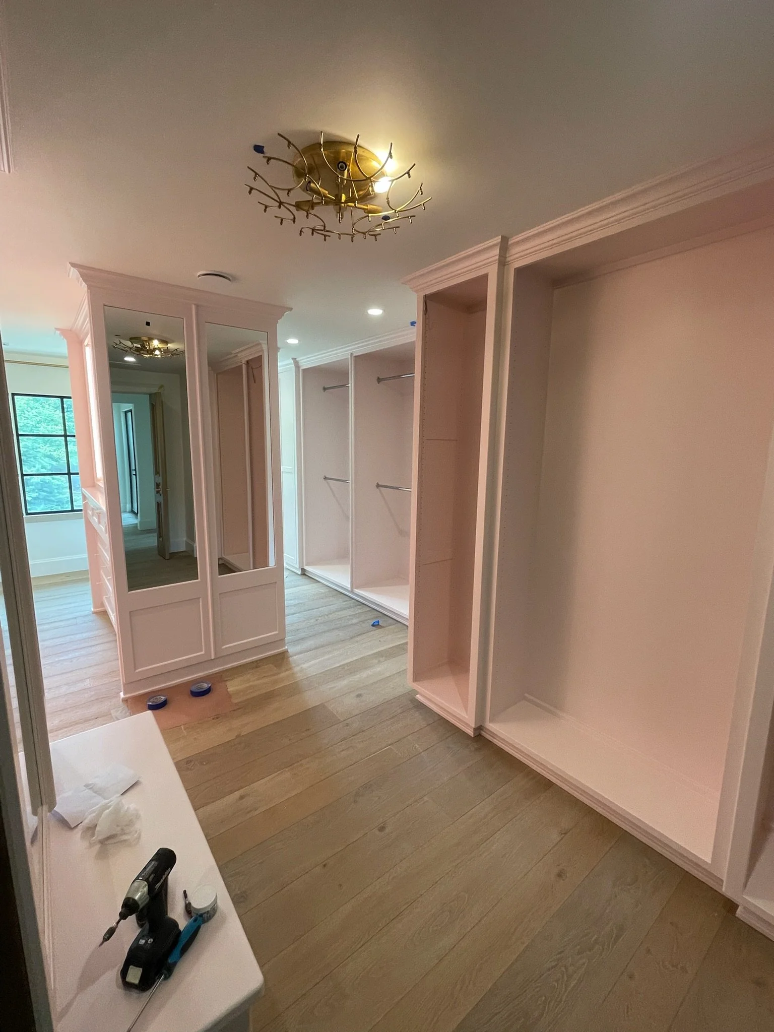 Empty closet with built-in shelves and a mirror, unfinished with tools on a white table in the foreground.