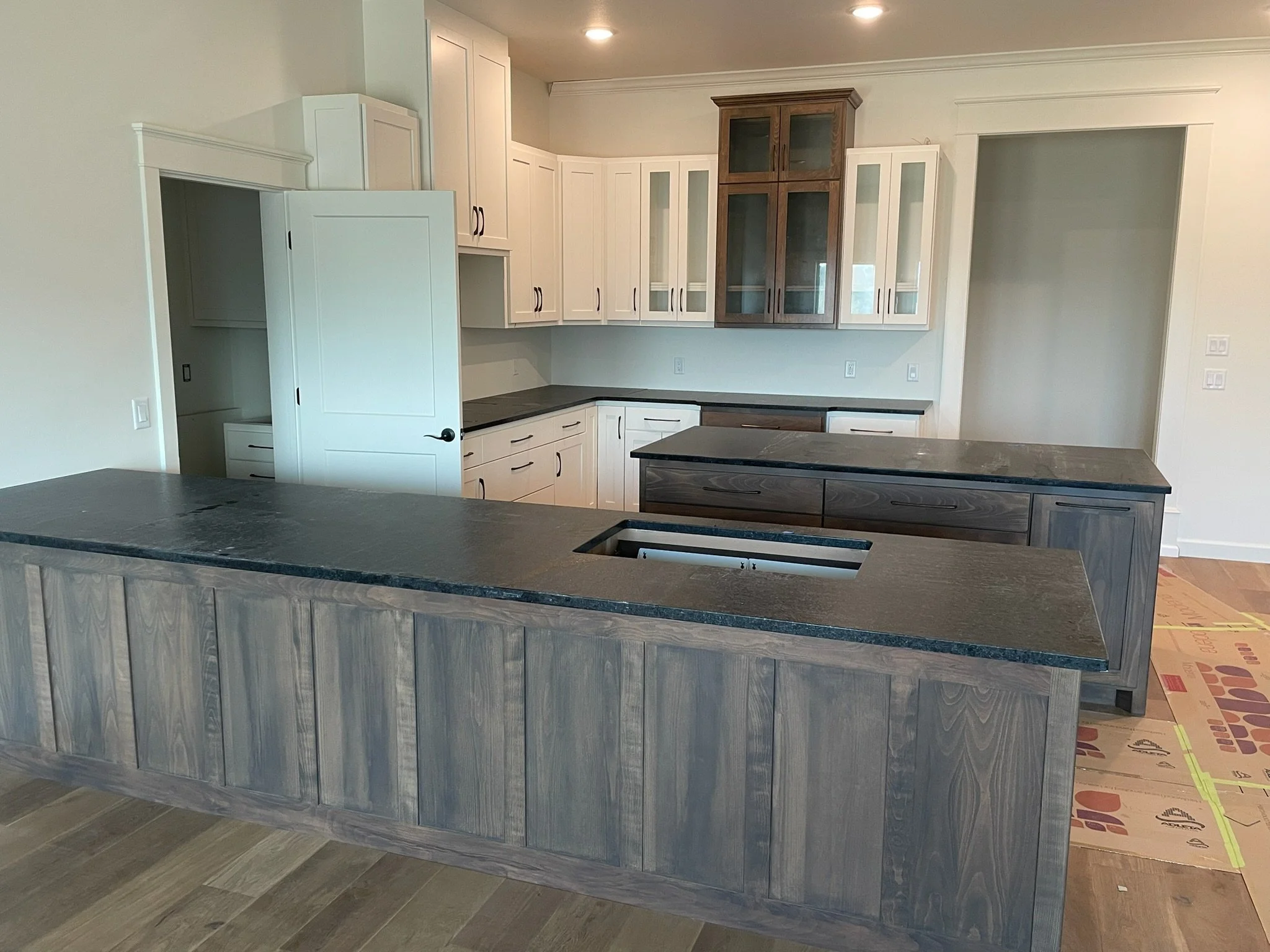 Kitchen with black countertops, white cabinets, and a central island with a dark wood base, adjacent to dining area with hardwood floors.