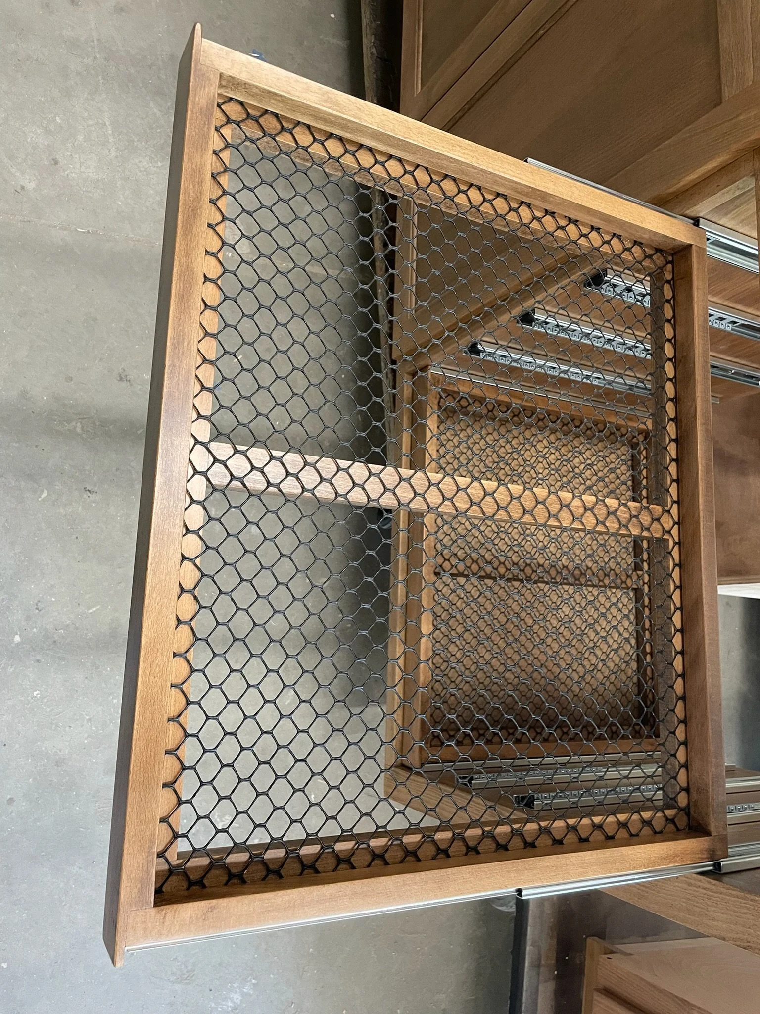 Wooden table with metal honeycomb wire mesh top, situated in a room with wooden furniture and a concrete floor.