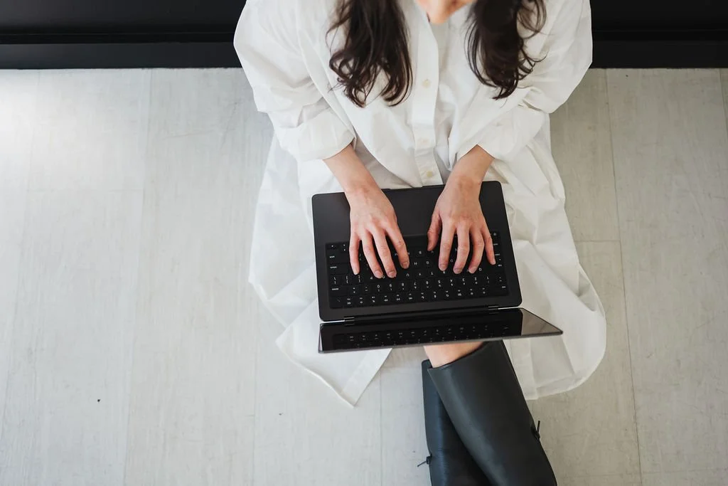 Photo of woman in white dress sitting on floor with black laptop