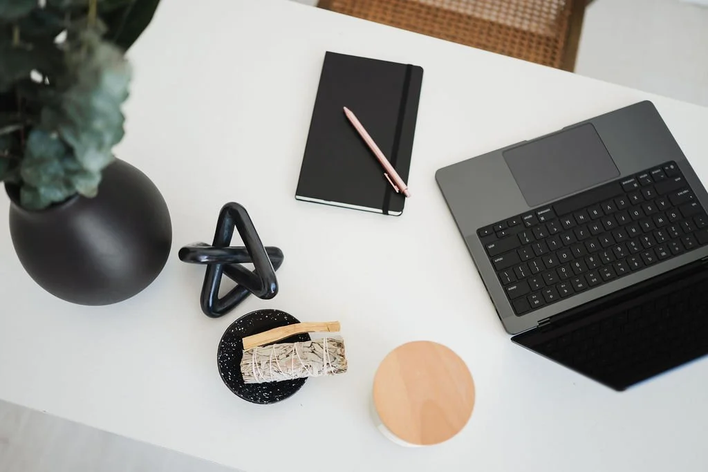 Photo of black laptop with sage and journal on white desk