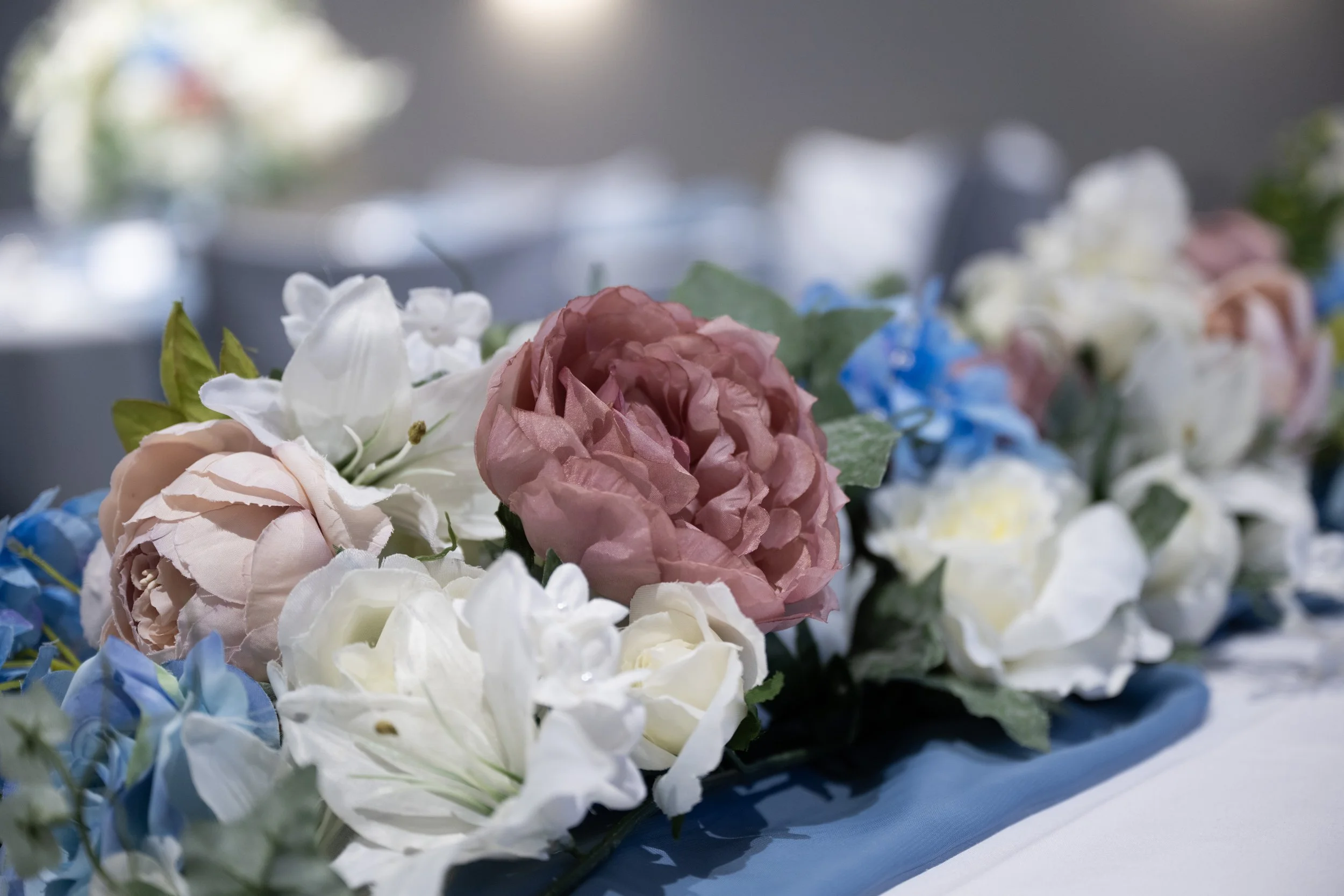 A close-up of a floral arrangement with pink, white, and blue flowers on a blue table runner.