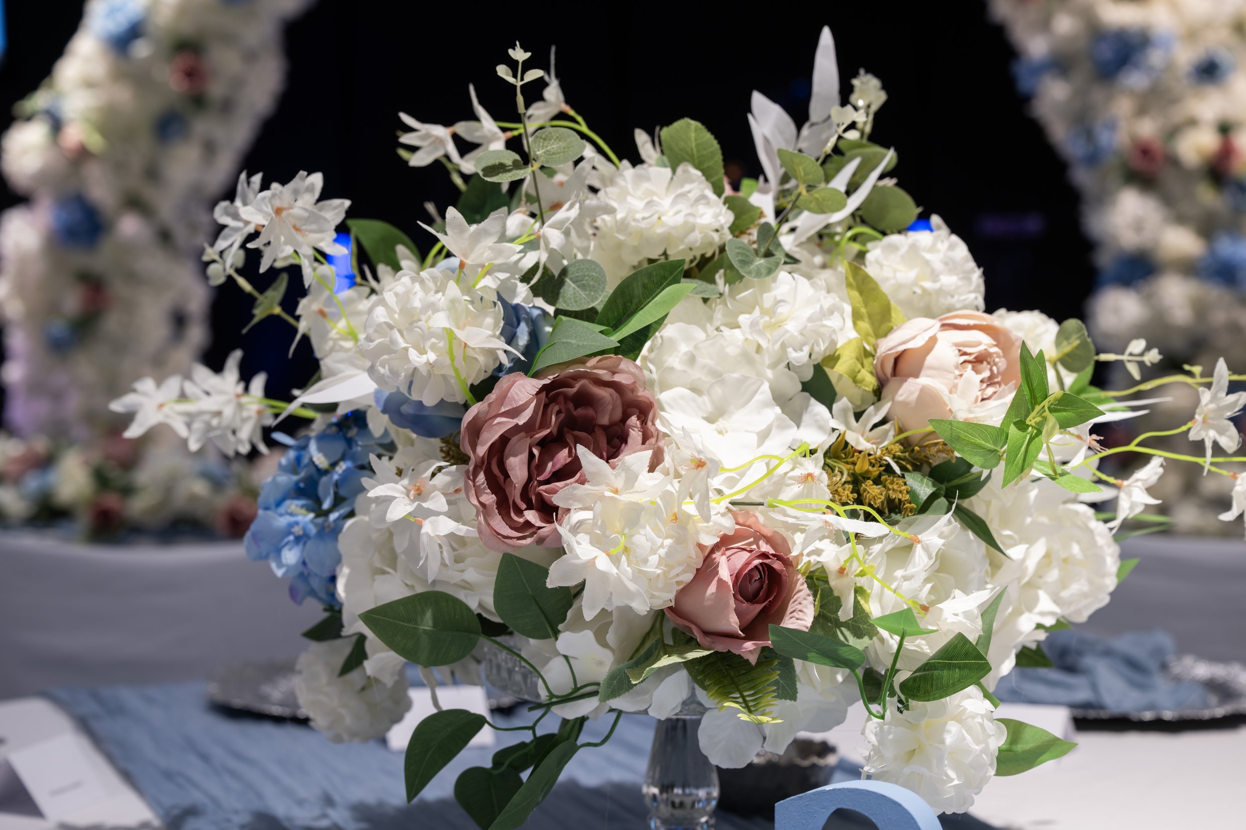 A floral arrangement of white, pink, and purple artificial flowers with green leaves in a silver vase.
