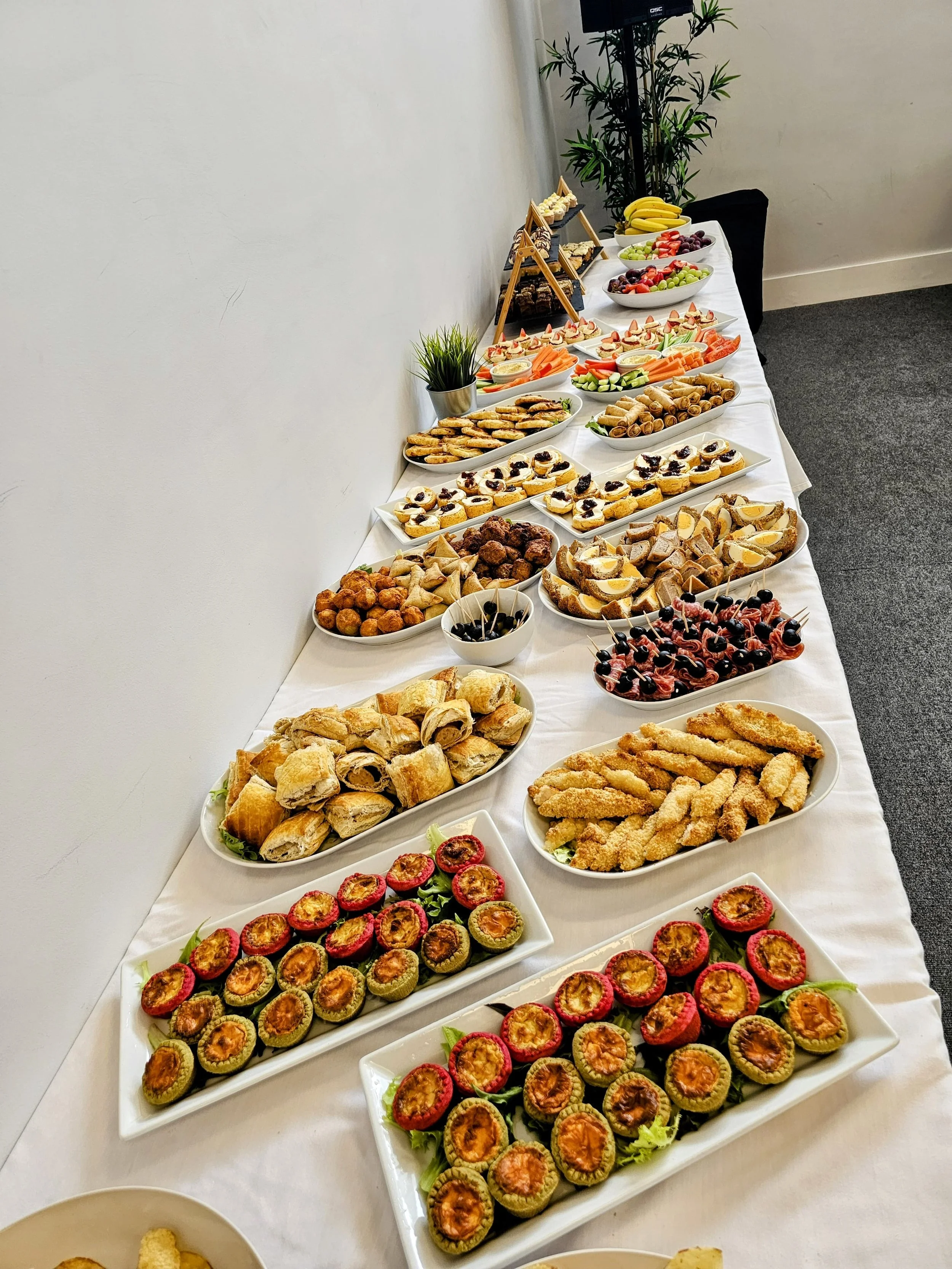 A long table covered with a white tablecloth displaying various appetizers, finger foods, and desserts at a party or event.