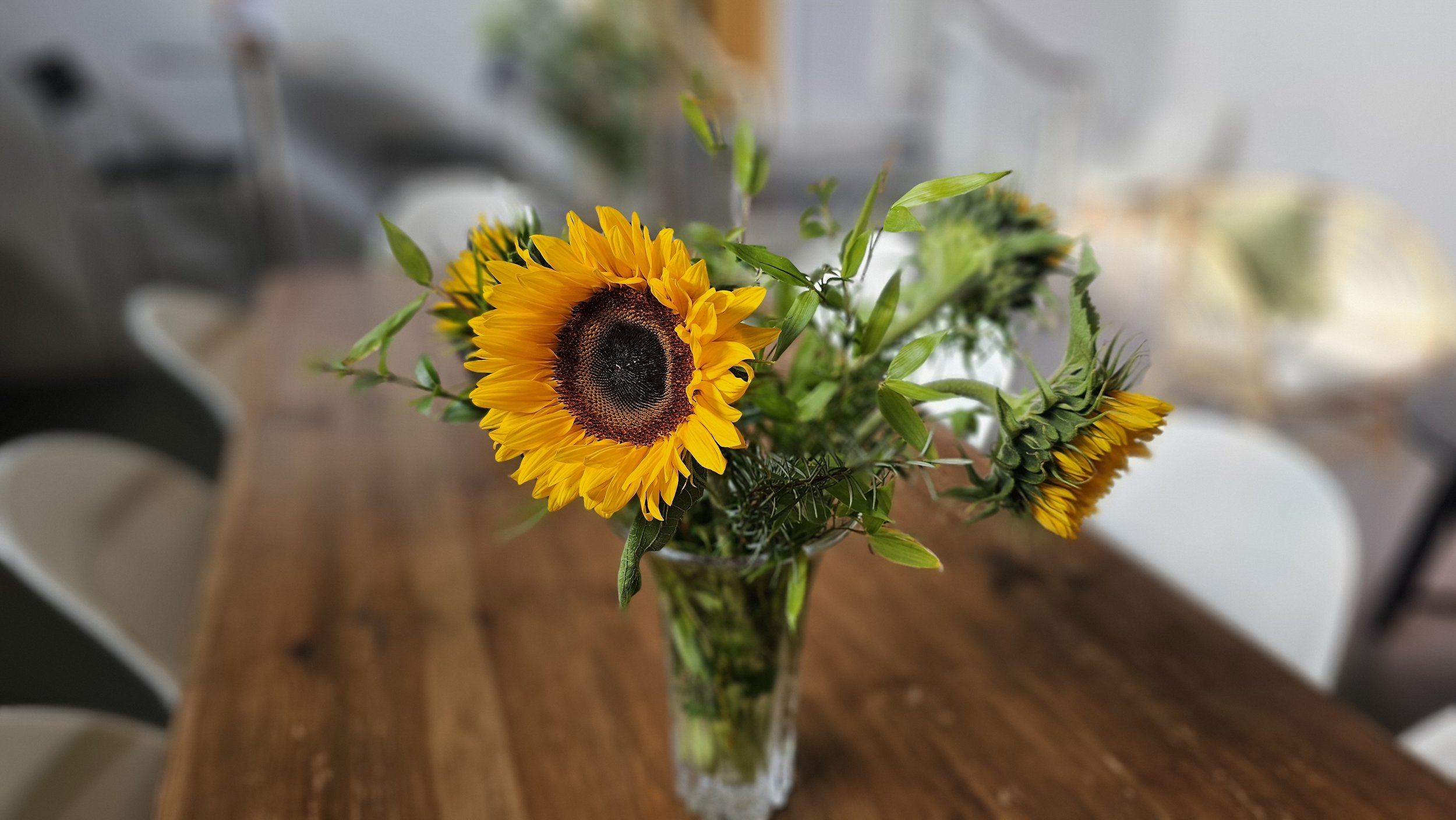 Sunflower bouquet in a glass vase on a wooden table in a modern kitchen or dining area.