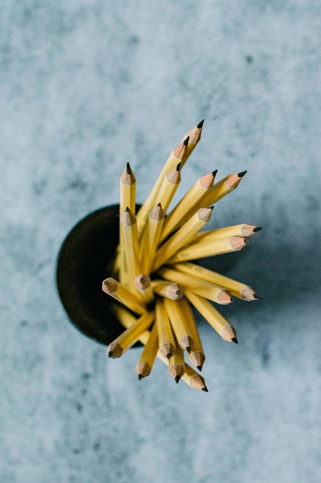 Top-down view of a black cup filled with yellow pencils on a gray surface.