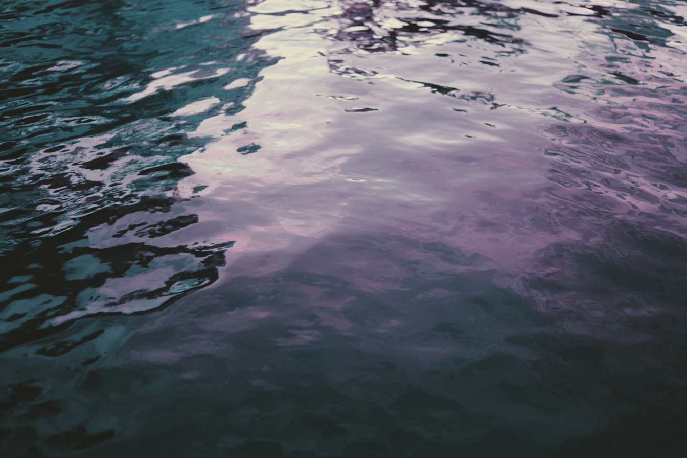 Close-up of water with ripples and reflections, showing shades of pink, purple, and blue.