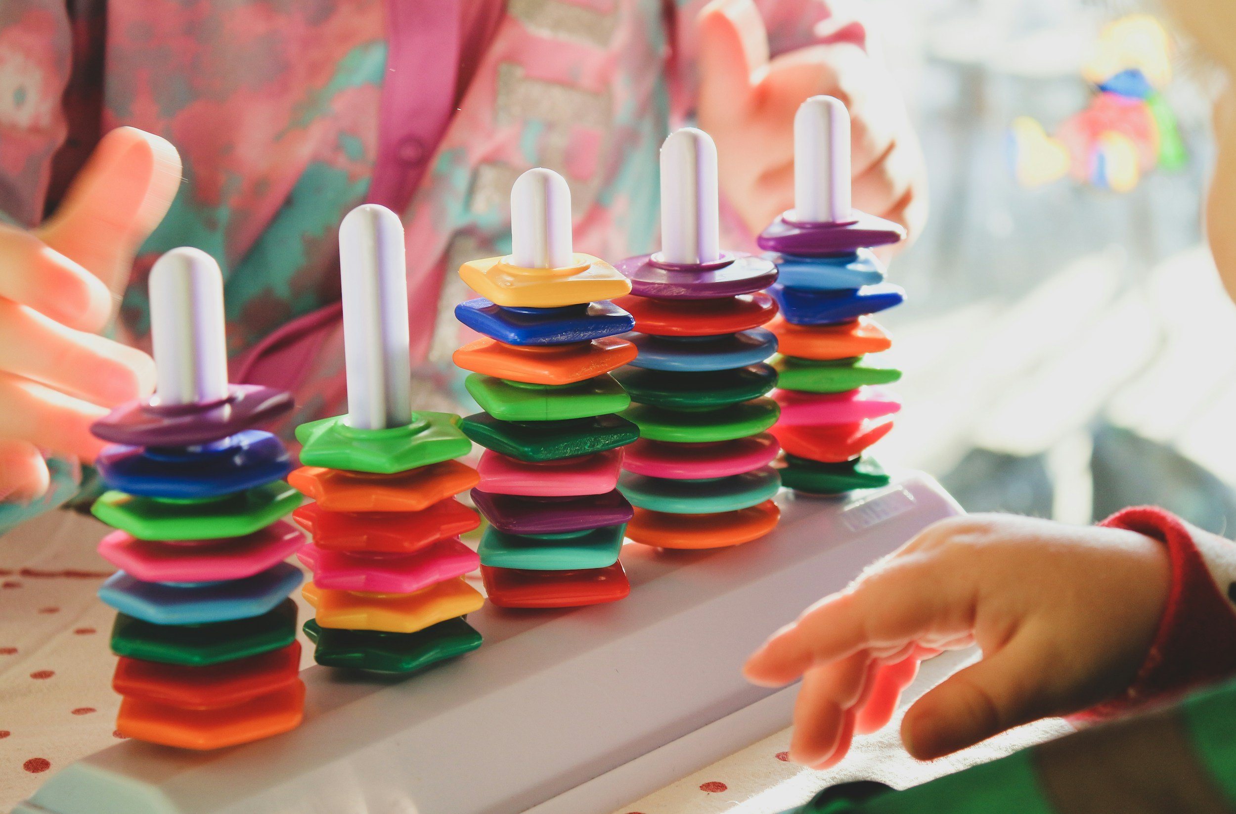 Child's hands stacking colorful plastic disks on white sticks to create a tower.