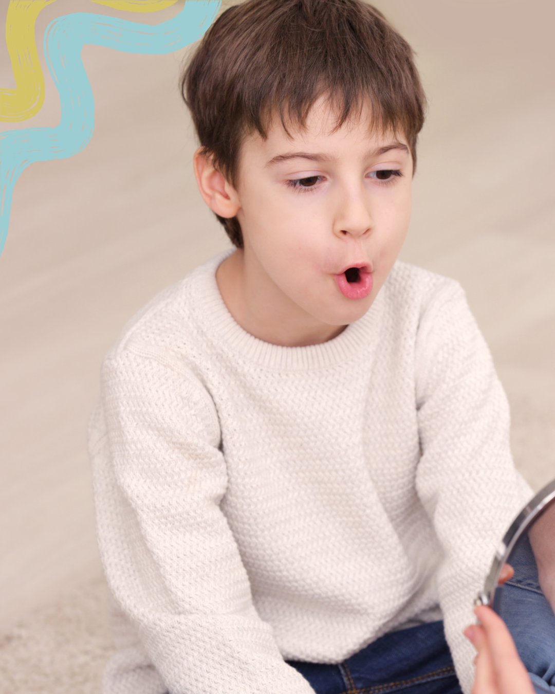 A young boy with brown hair, wearing a white knit sweater, looking at a mirror with a surprised expression.