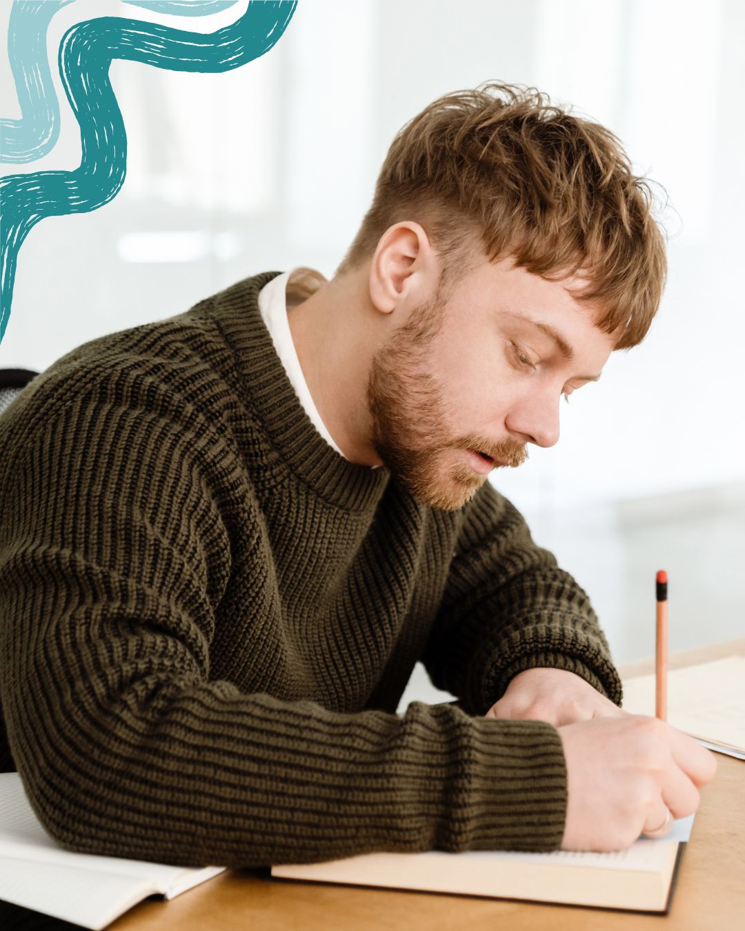 A young man with brown hair, beard, wearing a brown knit sweater, sitting at a desk, writing in a notebook with a pencil, in a bright room with white curtains.