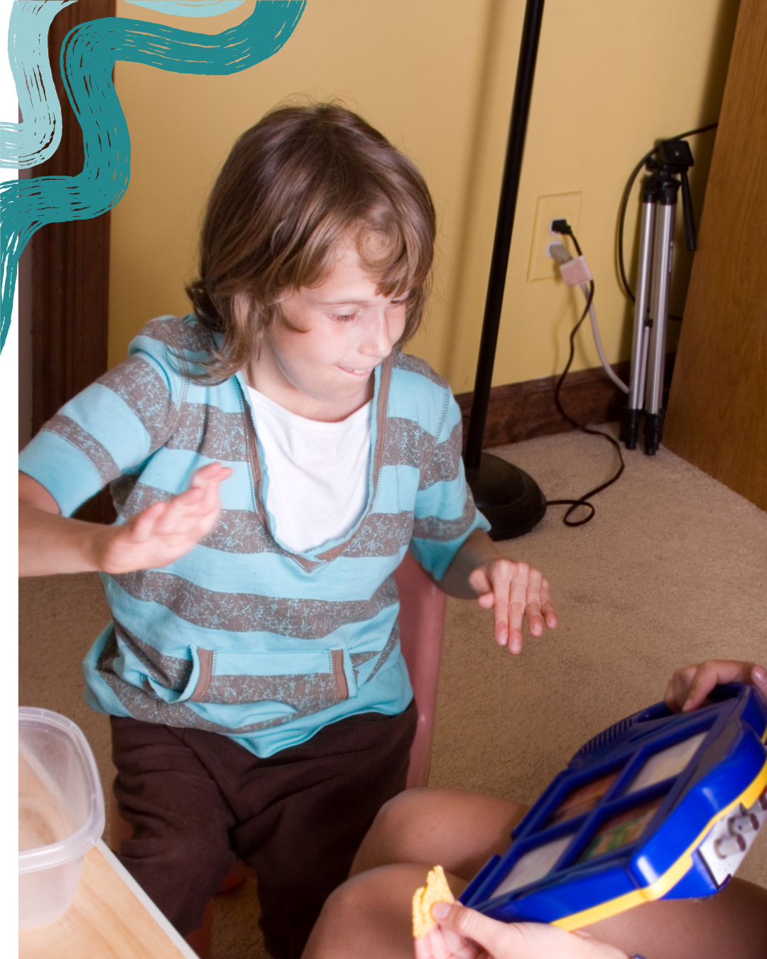 A young boy with brown hair, wearing a blue and gray striped hoodie and brown shorts, appears to be upset or crying, while sitting on a chair. Someone is holding a blue container with a sandwich, and another person is extending a hand towards the boy, possibly to comfort him. The scene is indoors with a yellow wall, a lamp, and an extension cord in the background.