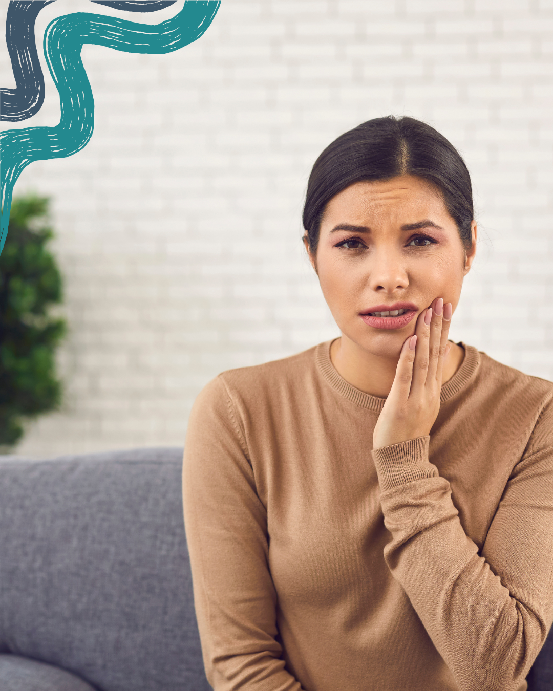 A woman sitting on a gray couch, touching her cheek with a worried expression, in front of a white brick wall with a decorative teal and black abstract element in the top left corner.