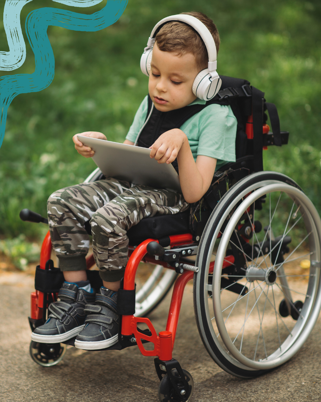 A young boy in a wheelchair wearing headphones, a green t-shirt, camo pants, and sneakers, is outdoors in a park, looking at a tablet.